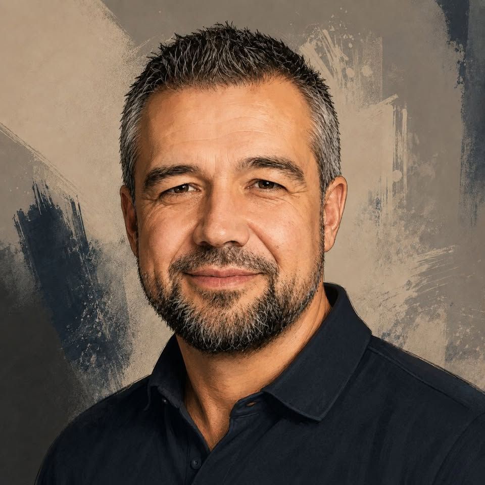 Professional headshot of a smiling middle-aged man with short dark hair and beard wearing a black polo shirt.