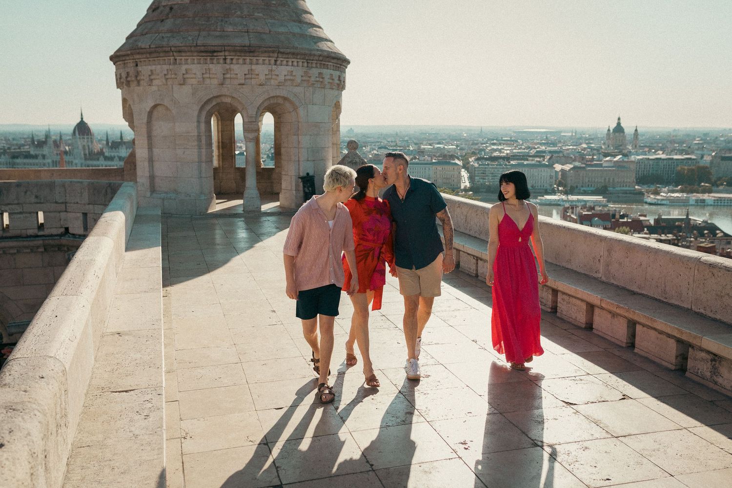 Family of four walking together, posing for their portraits. Mom and dad are kissing.