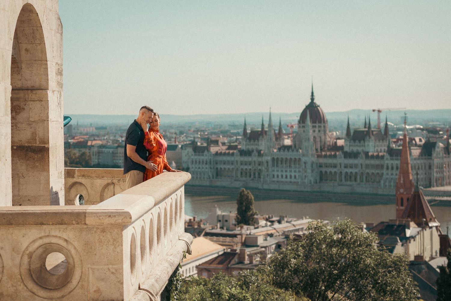 Couple cuddling, standing on the balcony of Fisherman's Bastion. The Danube and the Parliament building is in the background