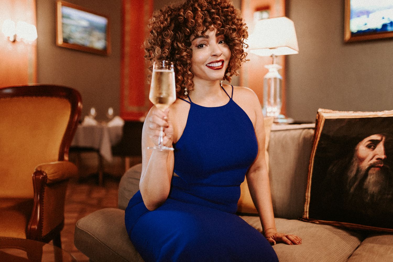 Elegant woman sitting on a couch with a glass of champaigne in her hand posing for the camera during her solo portrait photoshoot