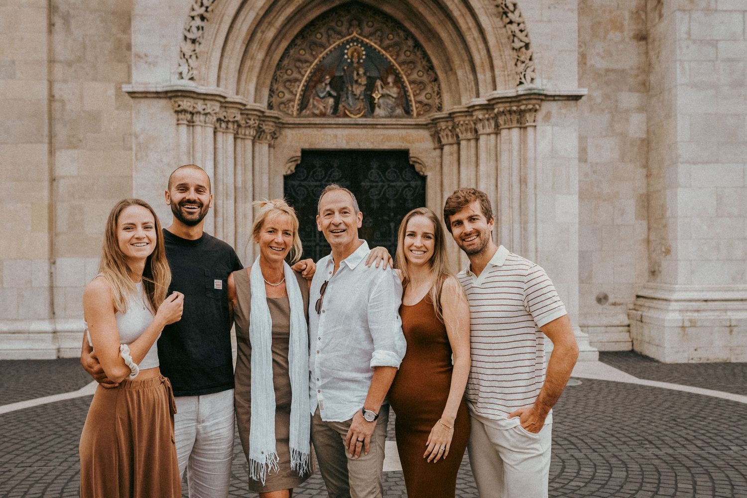 Family of six in front of Matthias Church in Budapest, looking in the camera for a group photo during their professional family photo shoot