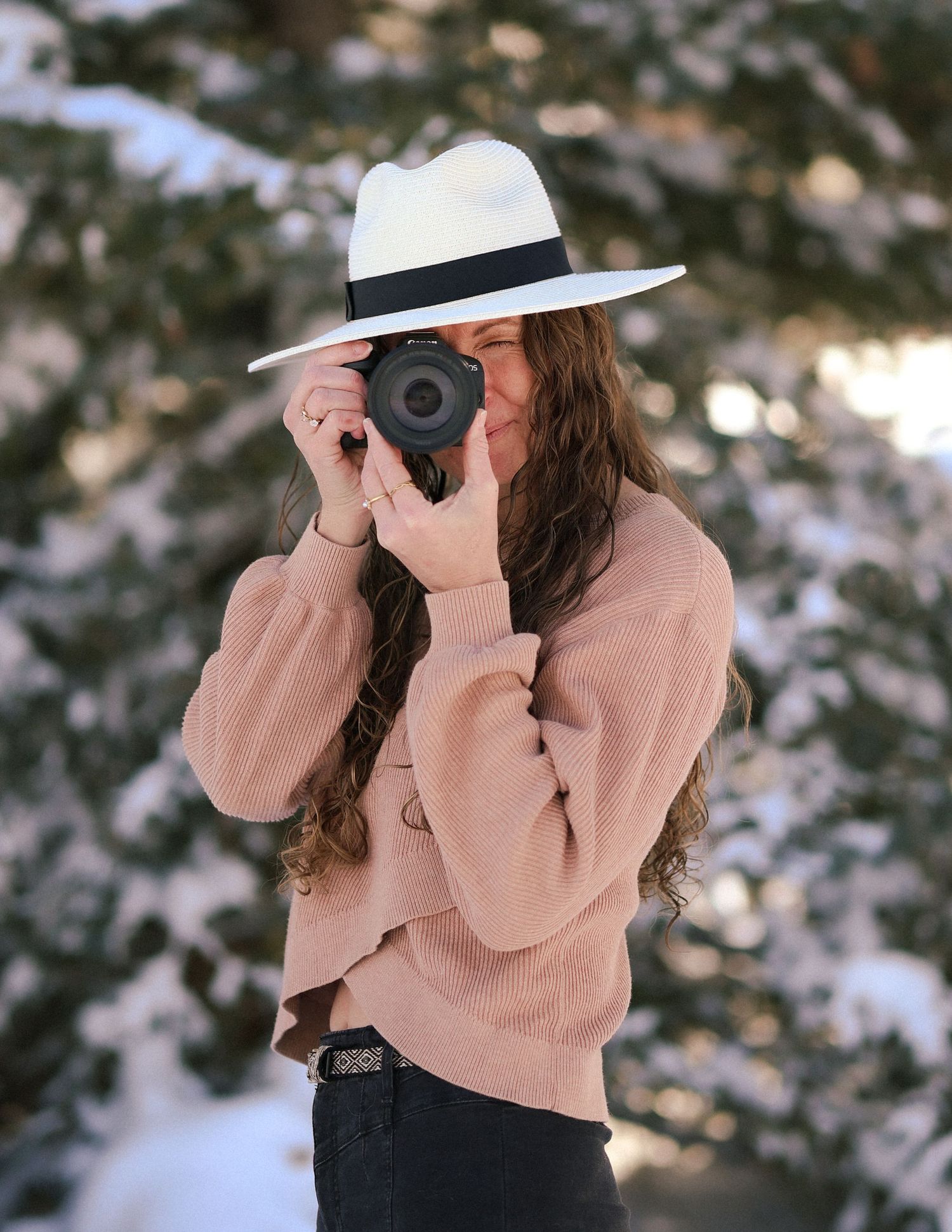 Woman with a hat on with a camera up to her face in a ready to capture a photo position