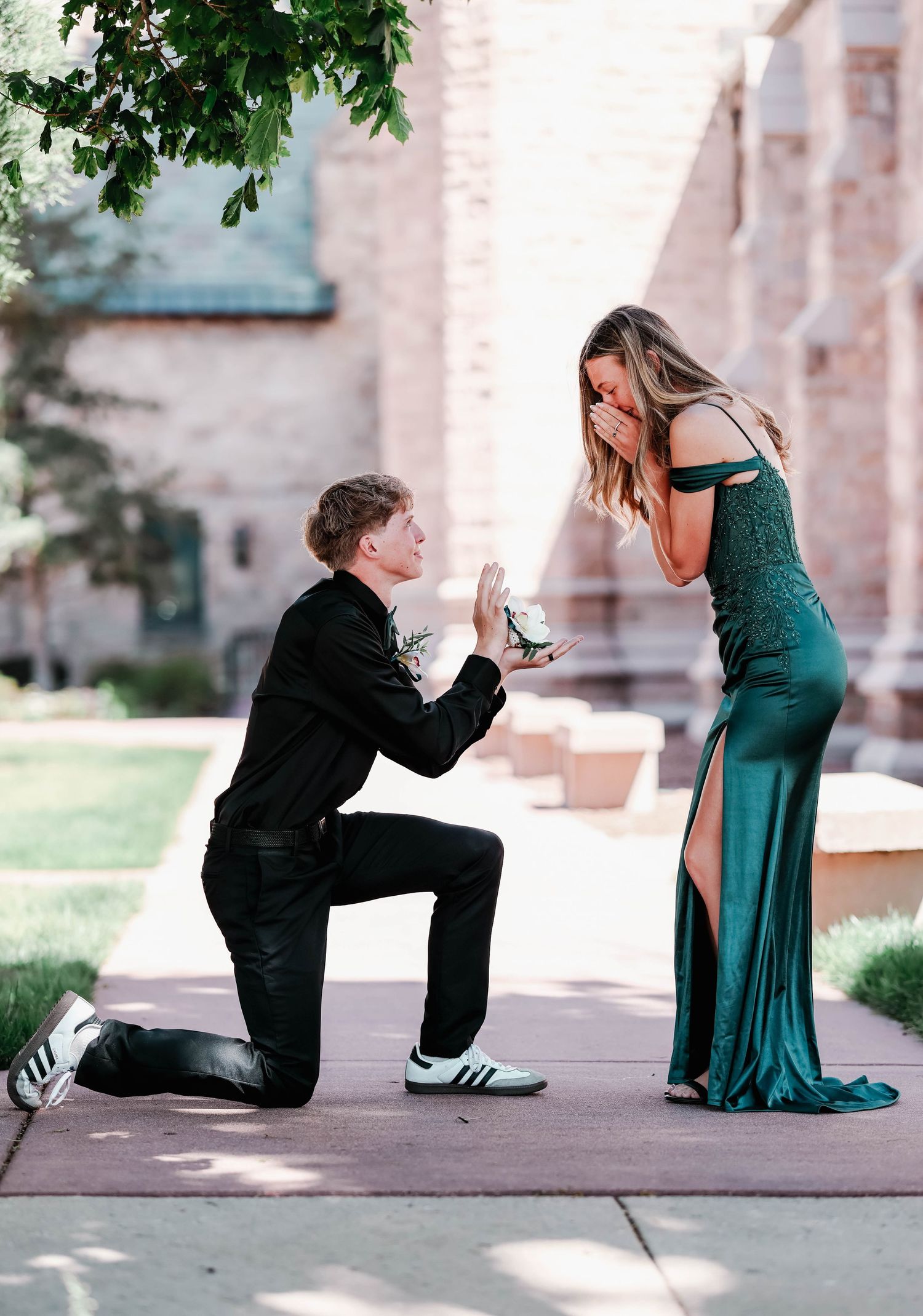 Couple in front of a church with boy down on one know simulating a proposal but with her corsage