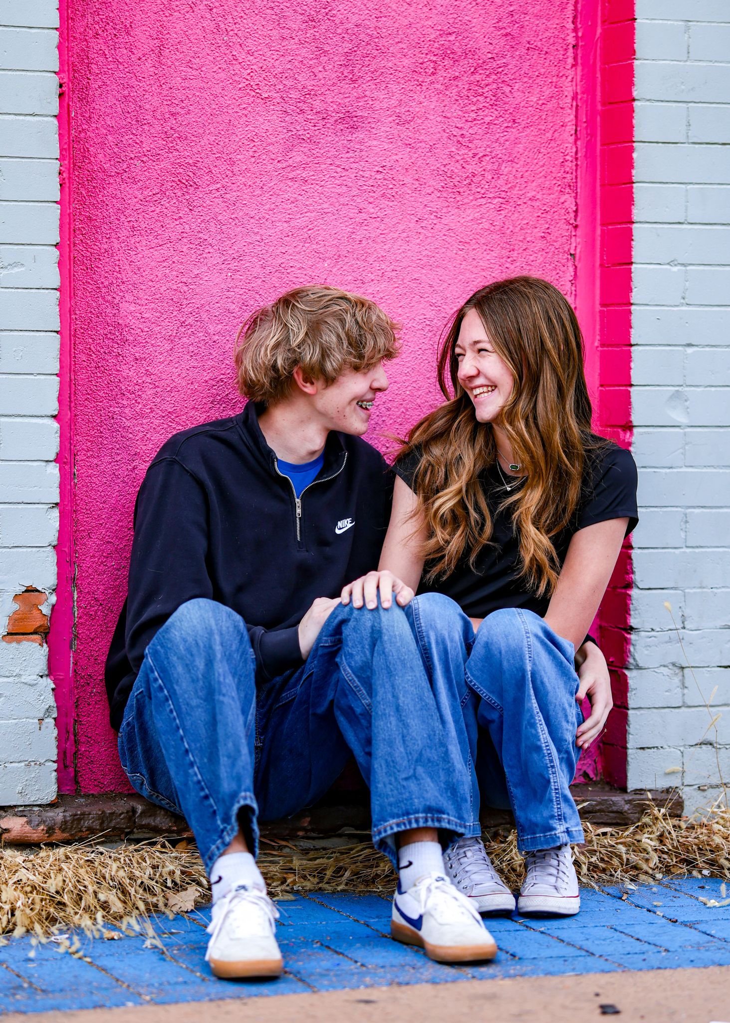 Young couple sitting against a hot pink painted building looking at each other