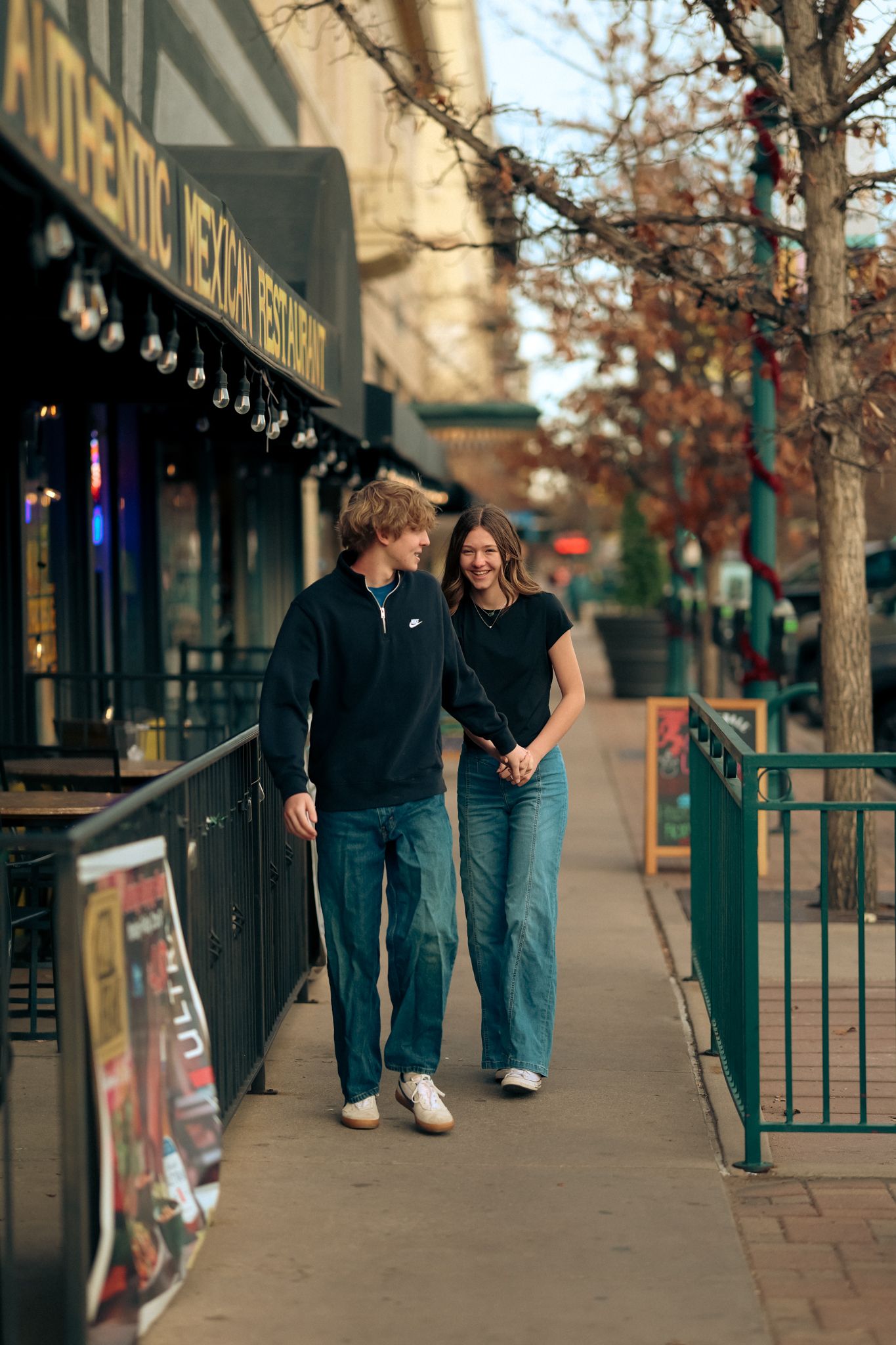 Young couple walking down a city street holding hands as they look at each other with smiles