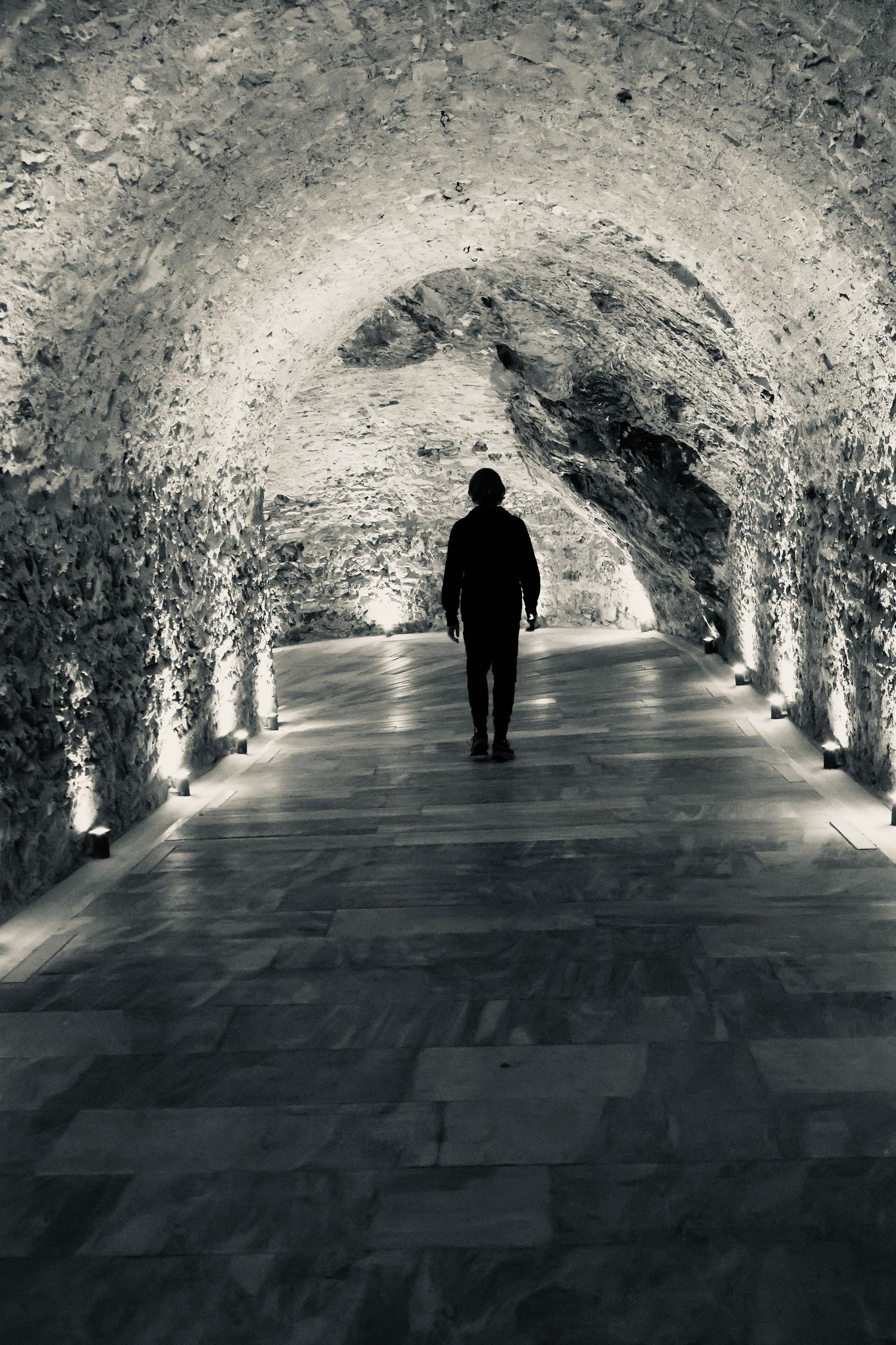 Young man walking down a brick tunnel lit with lights