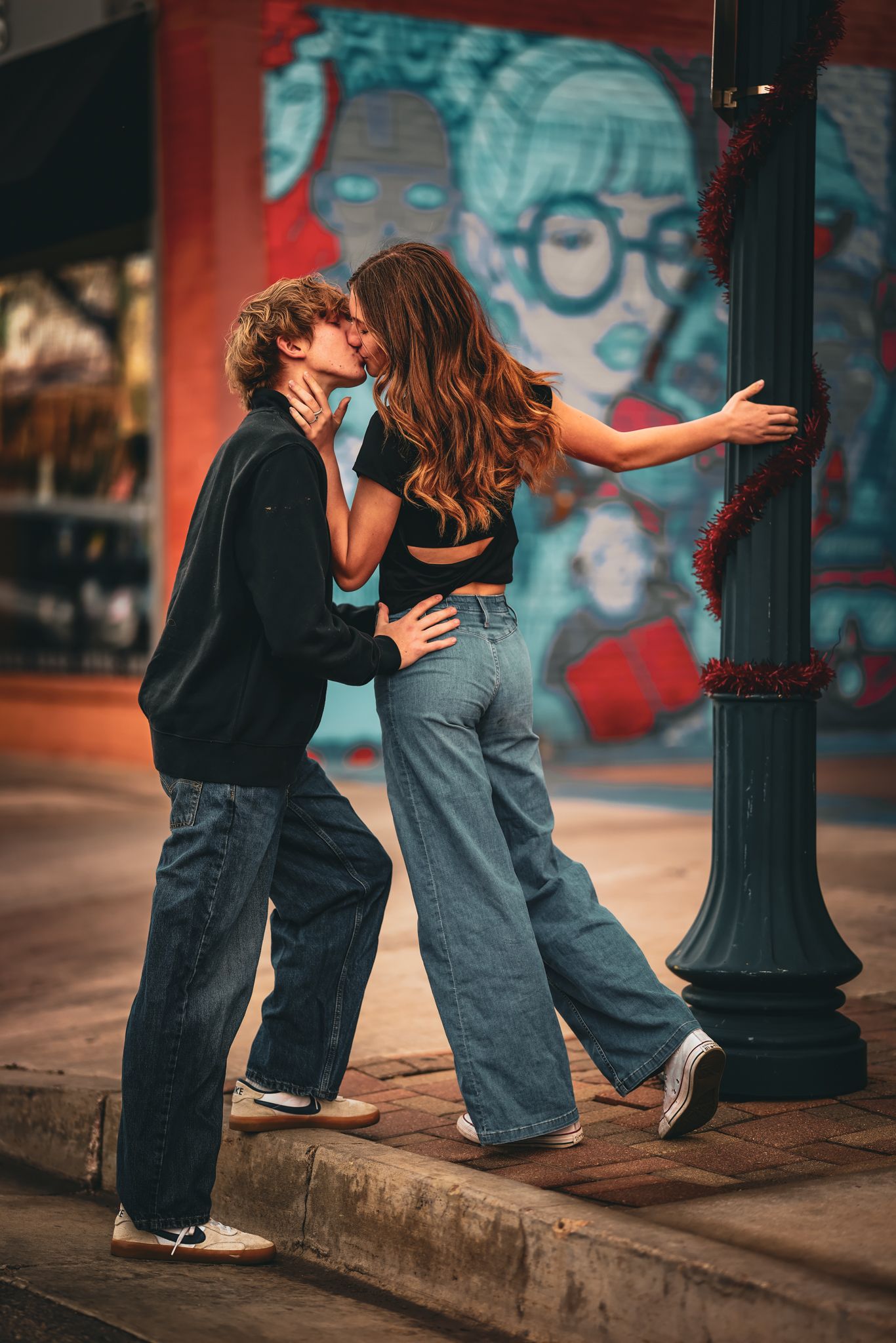 Young couple in a city landscape kissing as she leans into him while holding onto a light pole