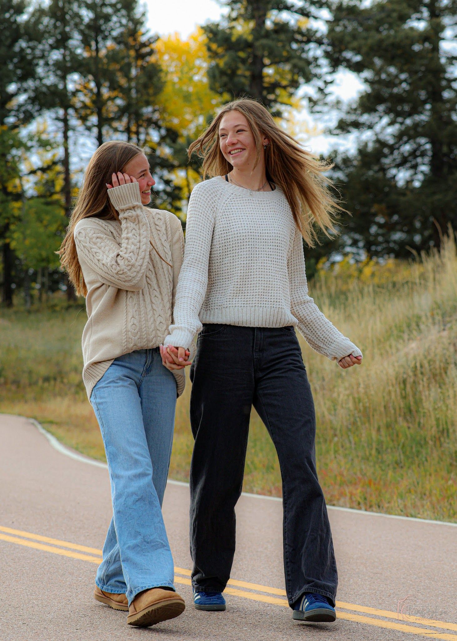 Two female friends walking down a street holding hands and laughing