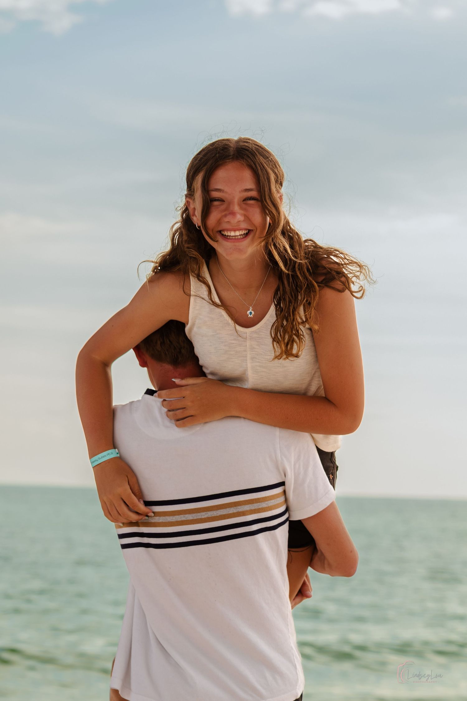 Young couple on a beach with young lady hoisted over his should as he walks away and she looks at the camera