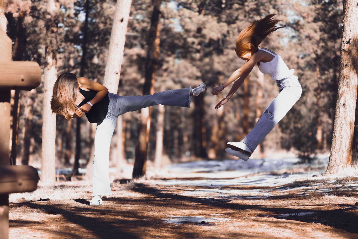 Two young ladies in an action shot with one girl's leg out pretending to kick the other as the other girl jumps into the air