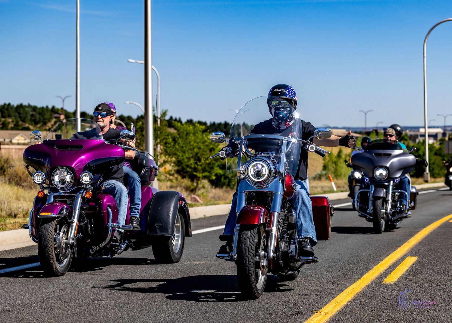 Three motorcycles and riders driving down the road