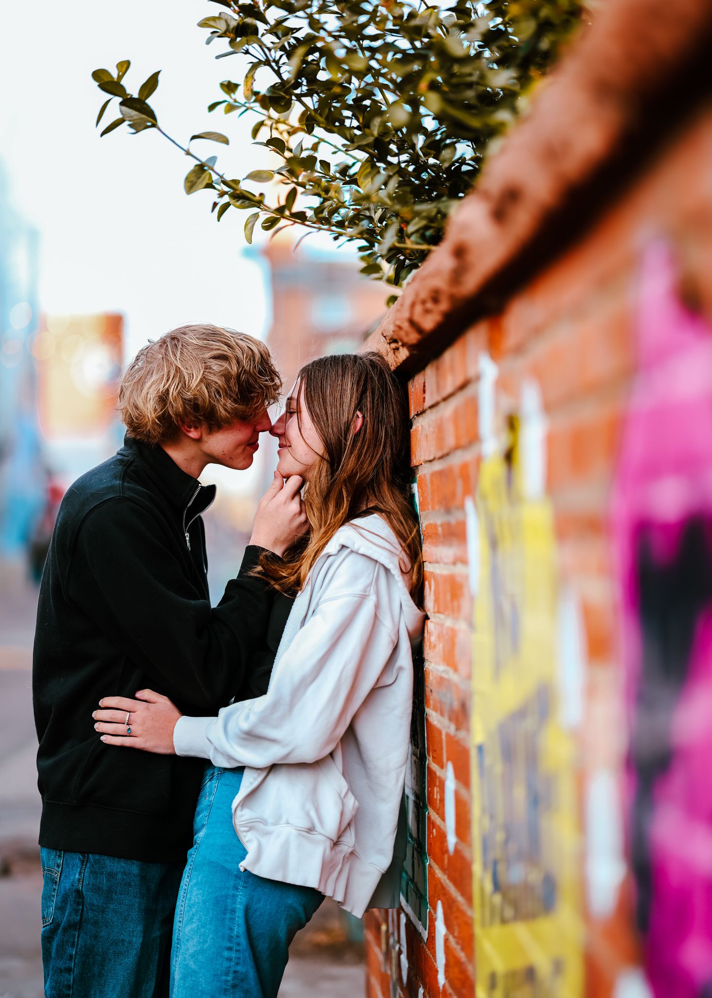 Young woman leaning her back against a brick wall as young man leans into her