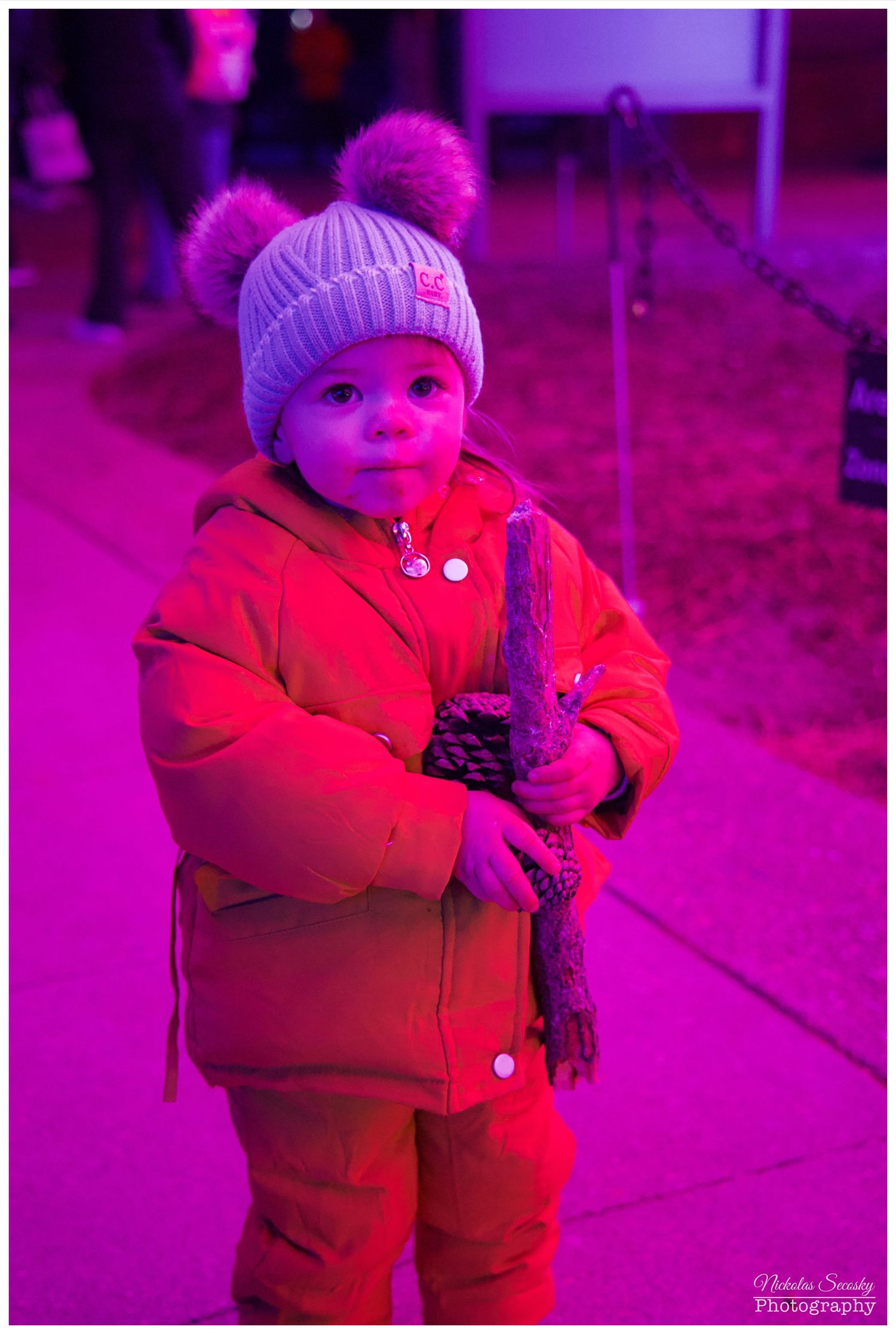 a small child in a yellow winter coat, carrying a stick and a pinecone