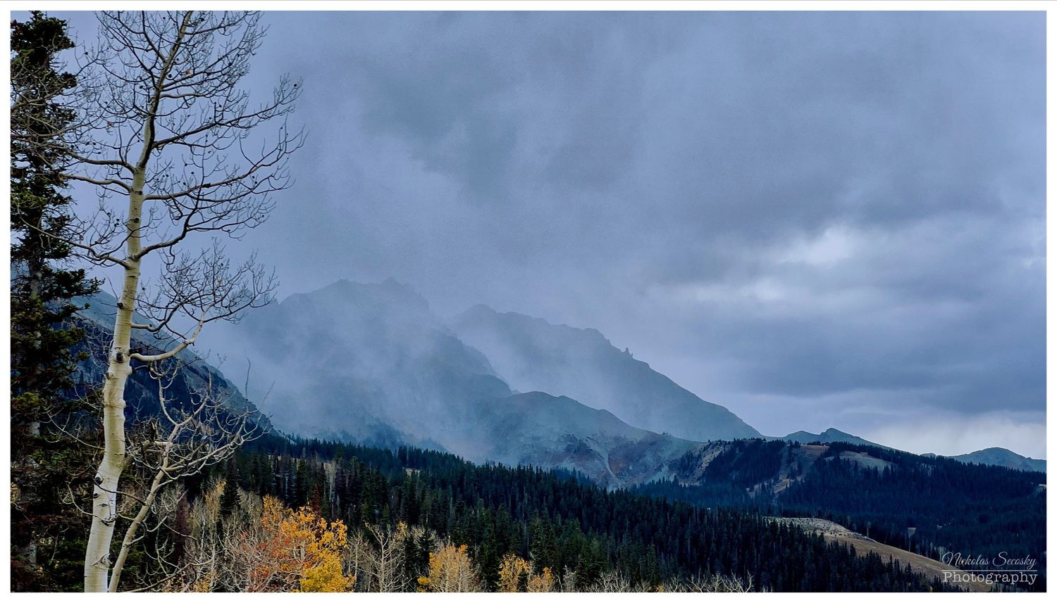 A landscape of mountains and trees with clouds coming in