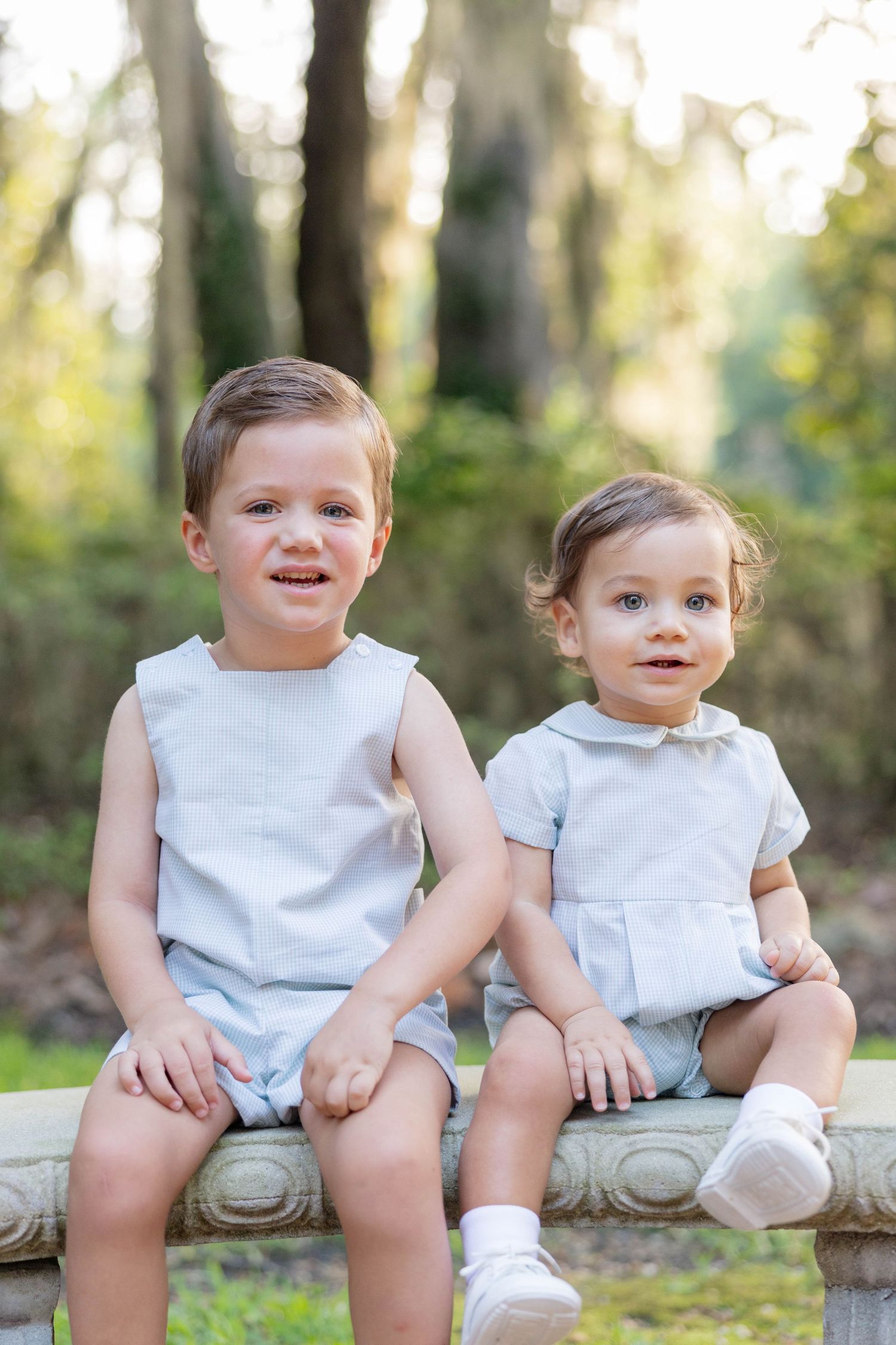 Two young toddlers in matching light blue outfits sitting together on a stone bench outdoors.