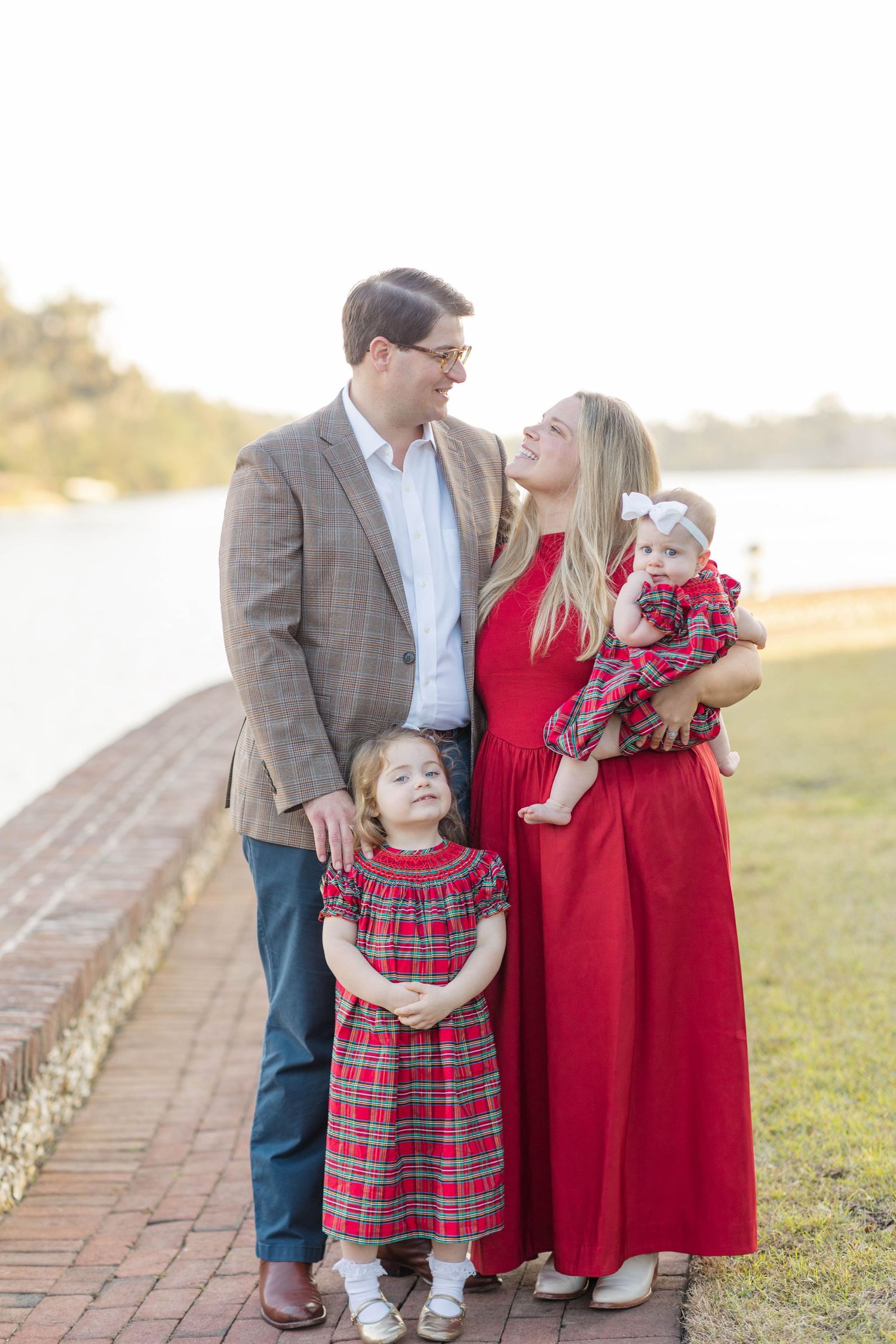 Family of four in red and plaid outfits posing outdoors near a waterfront at golden hour.
