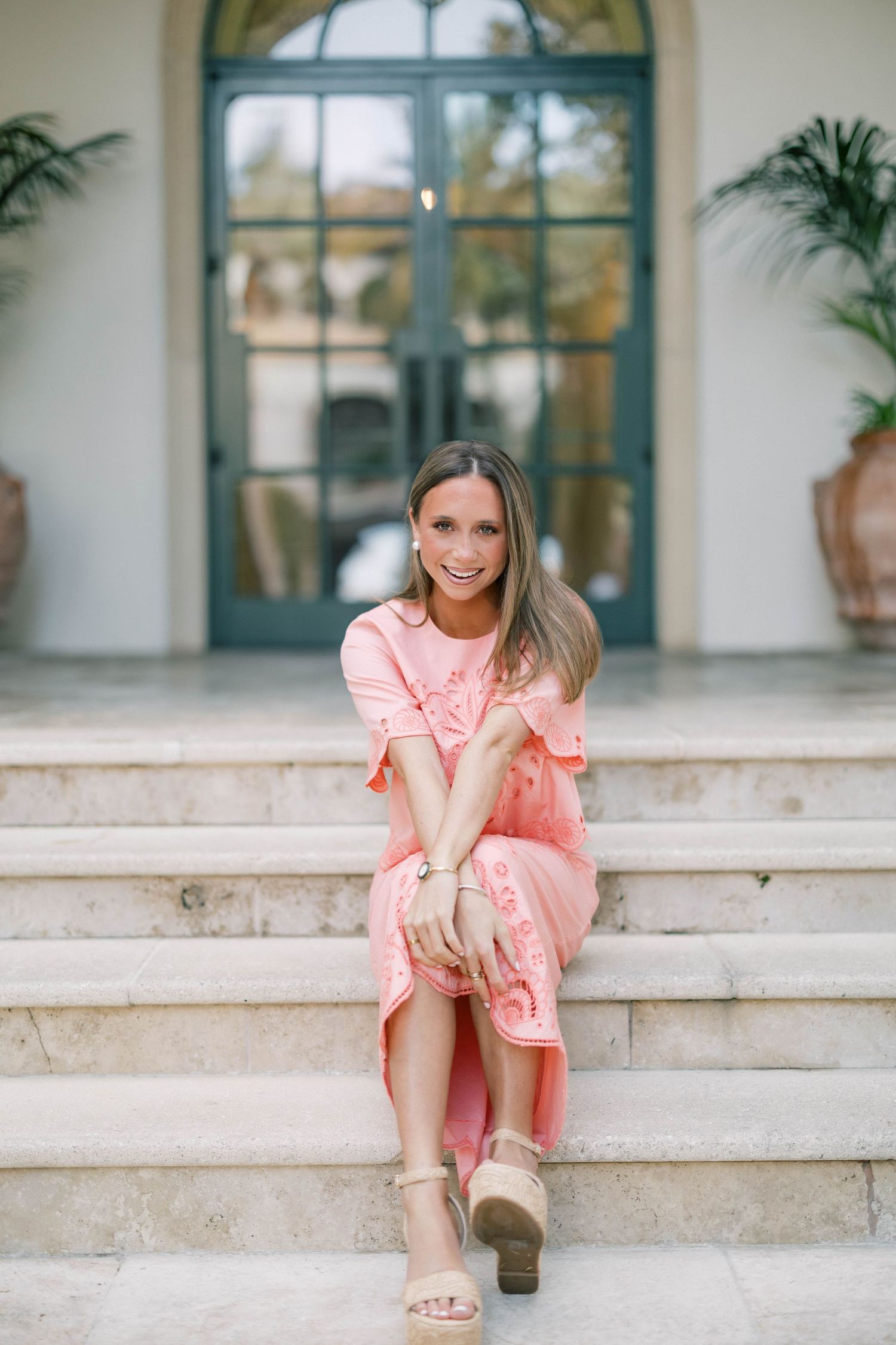 Woman in peach dress posing on outdoor stone staircase near arched windows.