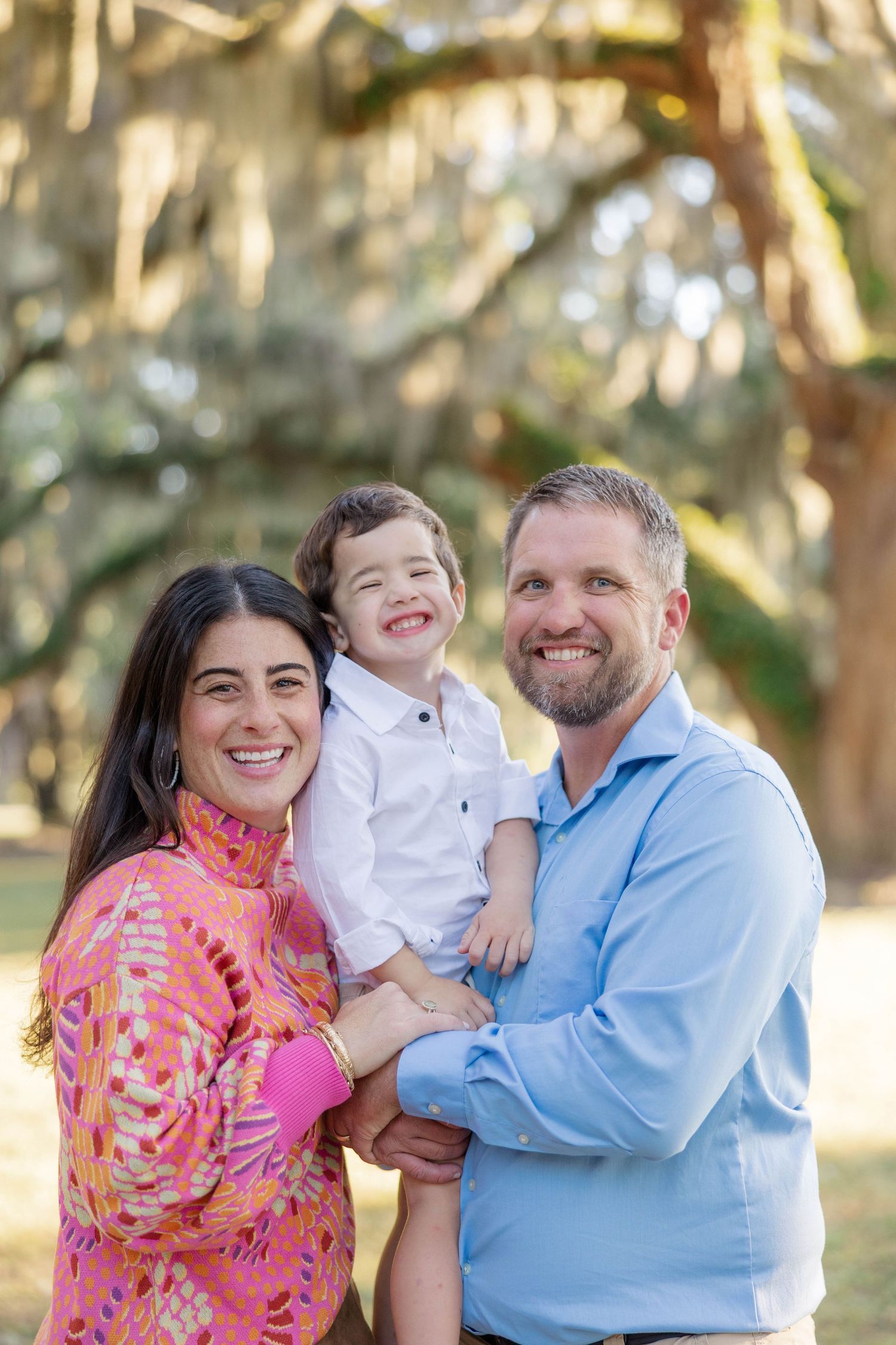 Happy family with young boy smiling outdoors under Spanish moss trees.