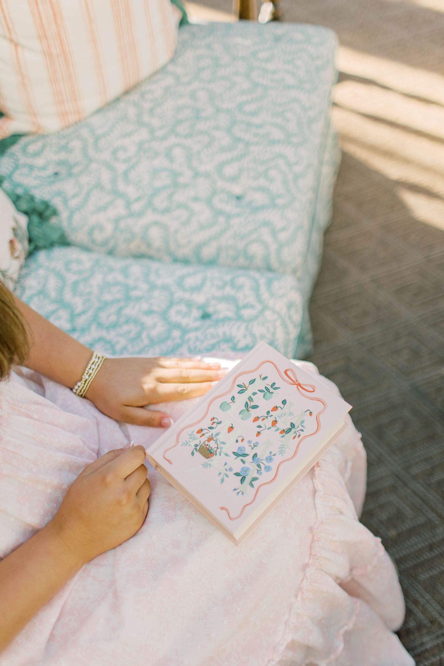 Bride in pink dress holds a floral illustrated wedding card while seated on a blue patterned sofa.