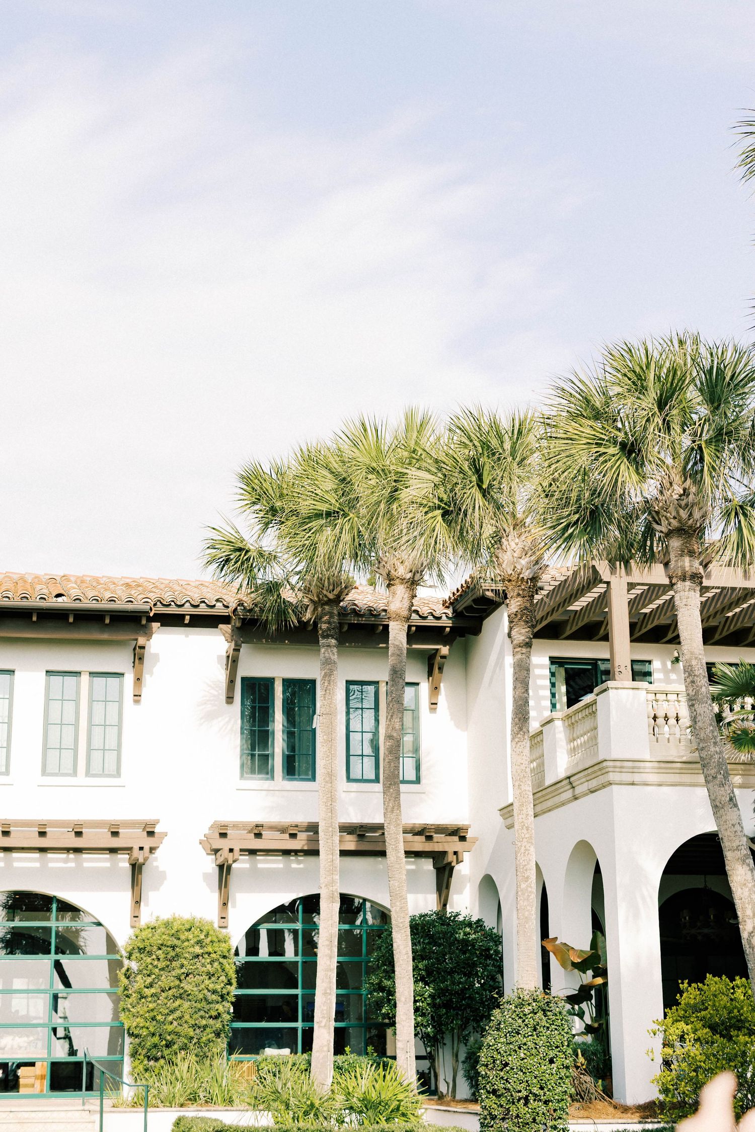 Mediterranean-style white building with green shutters and palm trees along the facade.