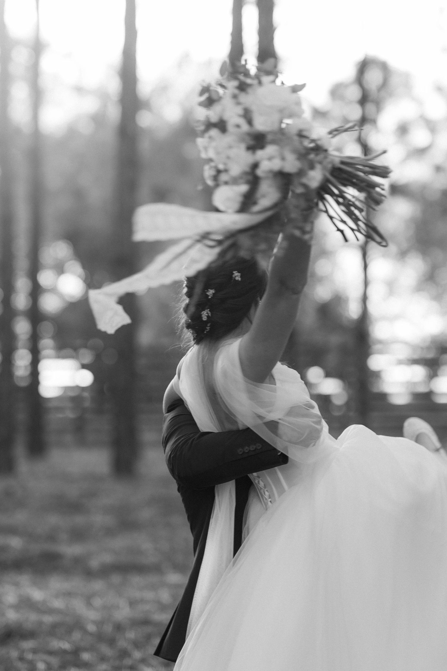 Black and white portrait of a bride in a flowing white dress with flowers in her hair in a forest setting.