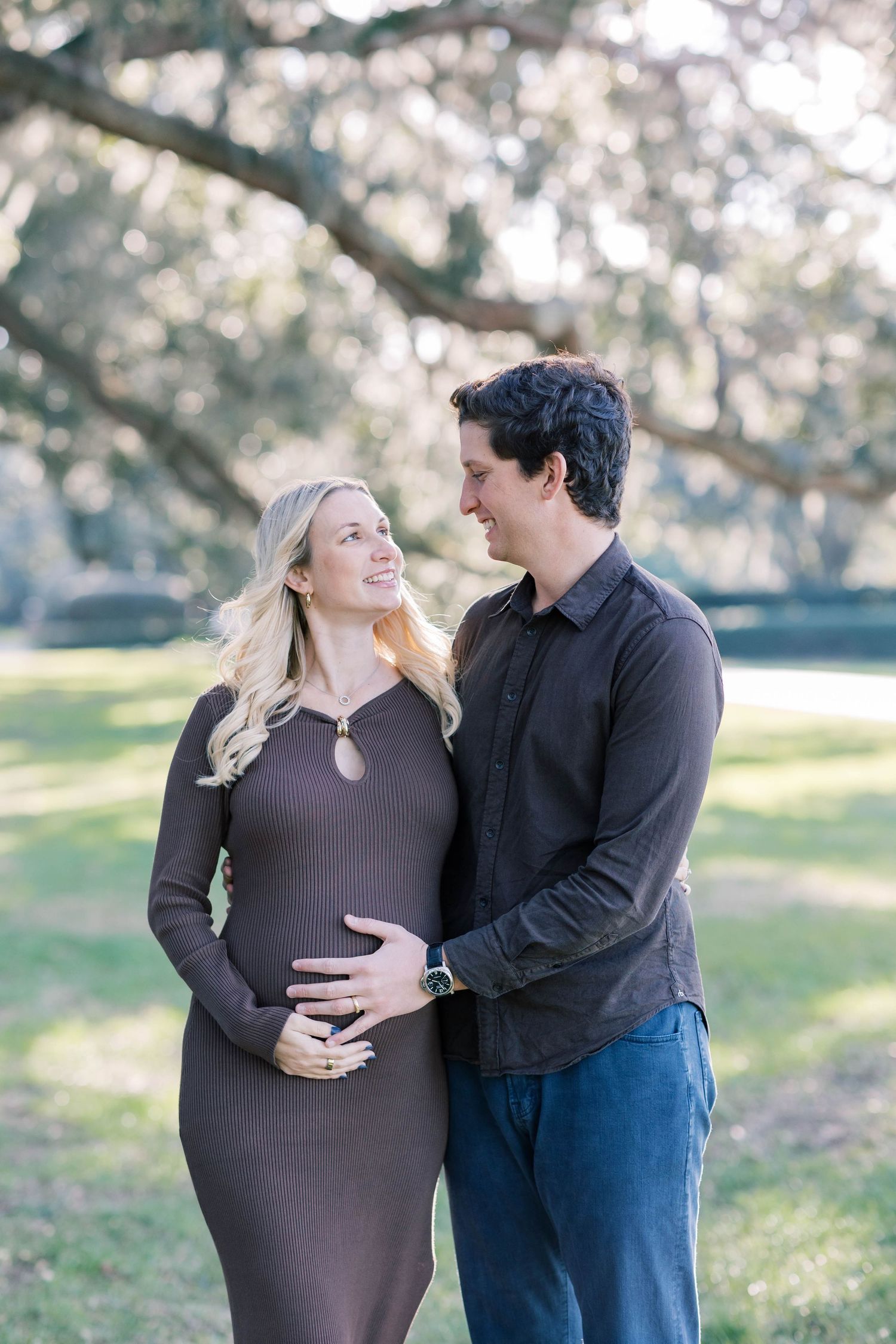 A couple shares tender moments during a maternity photo session in a sunlit outdoor setting.