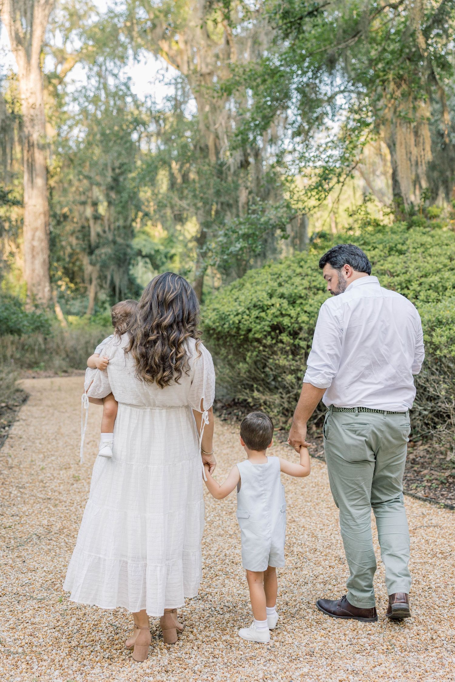Family of four walking on a gravel path surrounded by lush green trees draped with Spanish moss.
