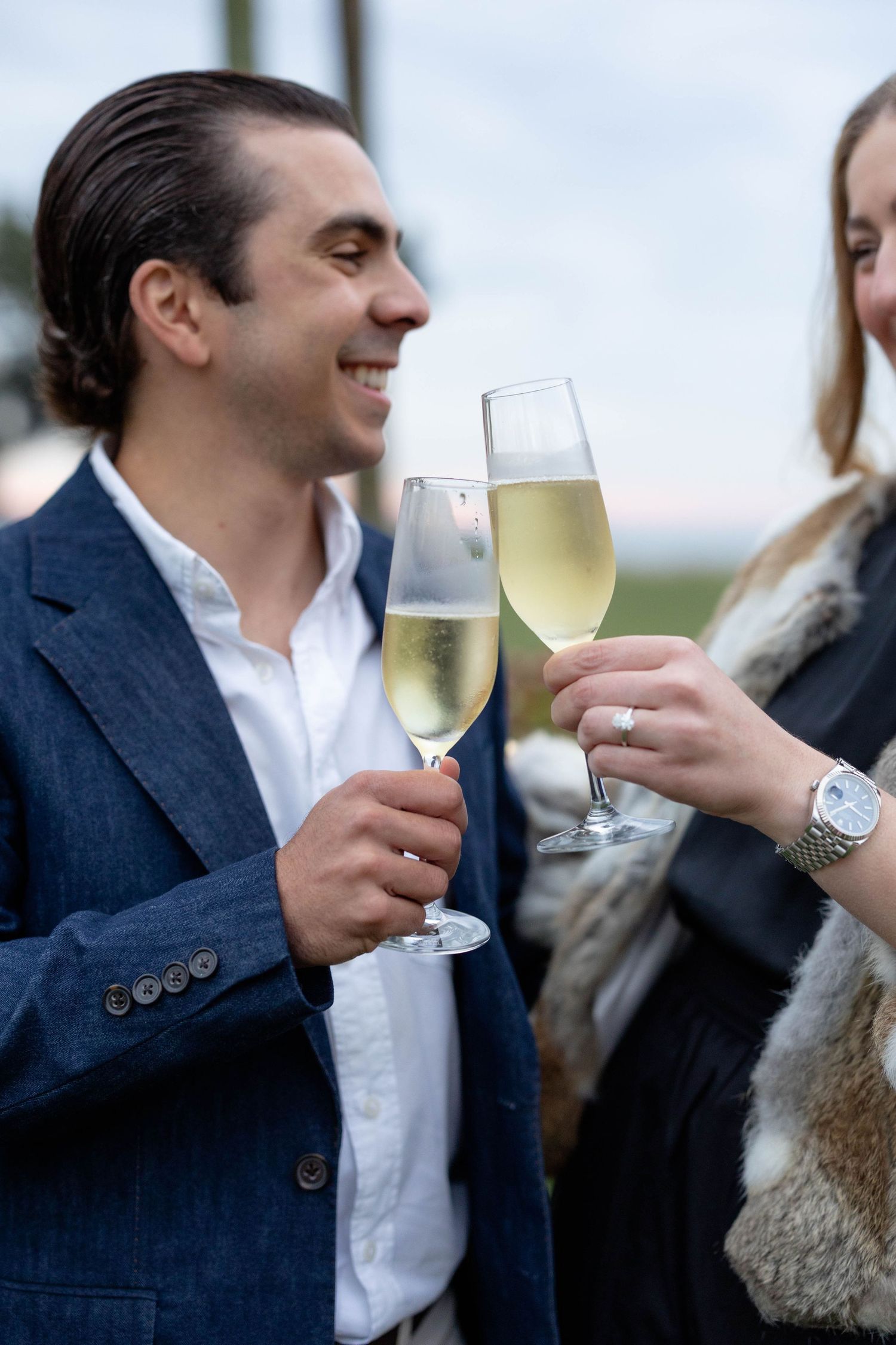 Two people in formal attire clink champagne glasses while sharing a cheerful moment at an event.