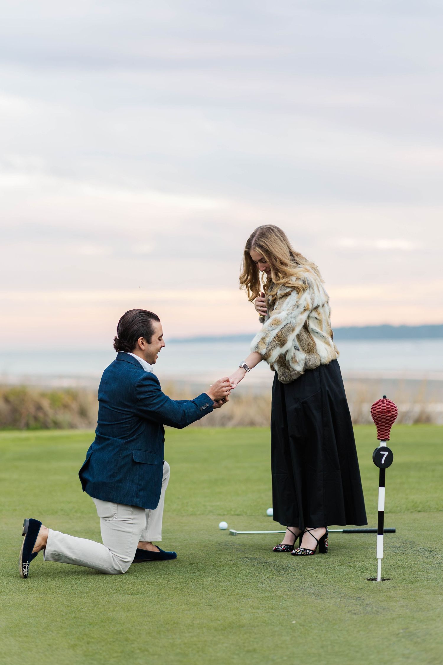 A romantic proposal takes place on a golf course at sunset with a person kneeling and offering a ring.