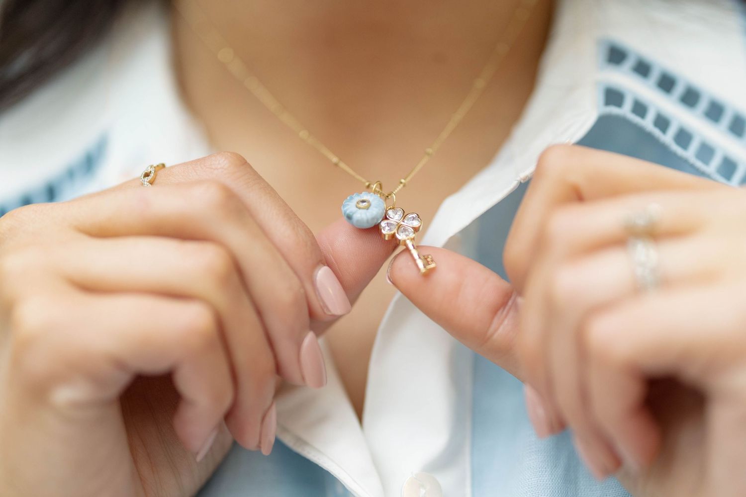 Woman holding a delicate gold necklace with a floral charm and blue gemstone pendant.