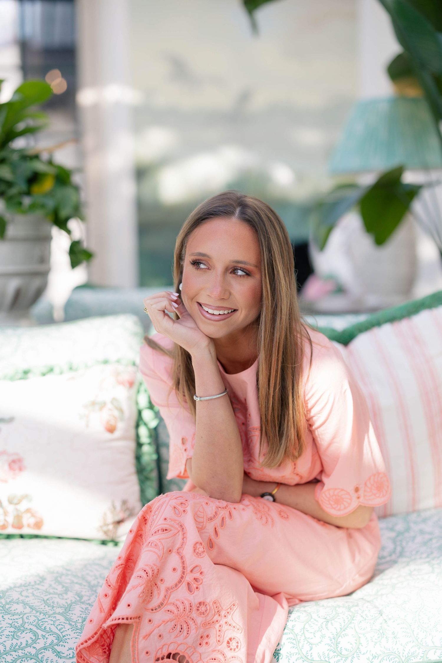 A person lounges on outdoor patio furniture wearing a peachy-pink dress in a garden setting.