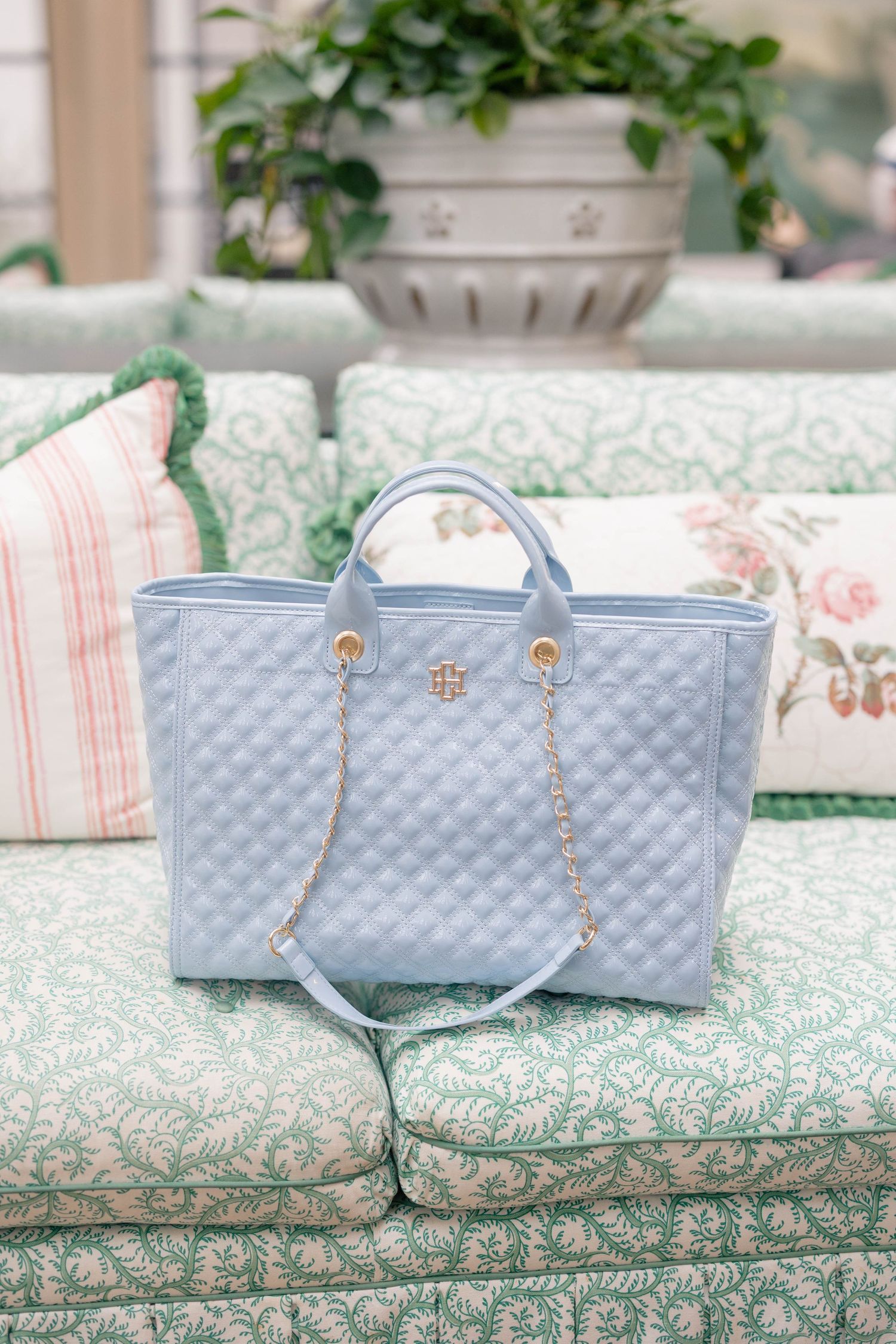 Light blue quilted Tory Burch tote bag with gold chain straps on a green floral sofa.