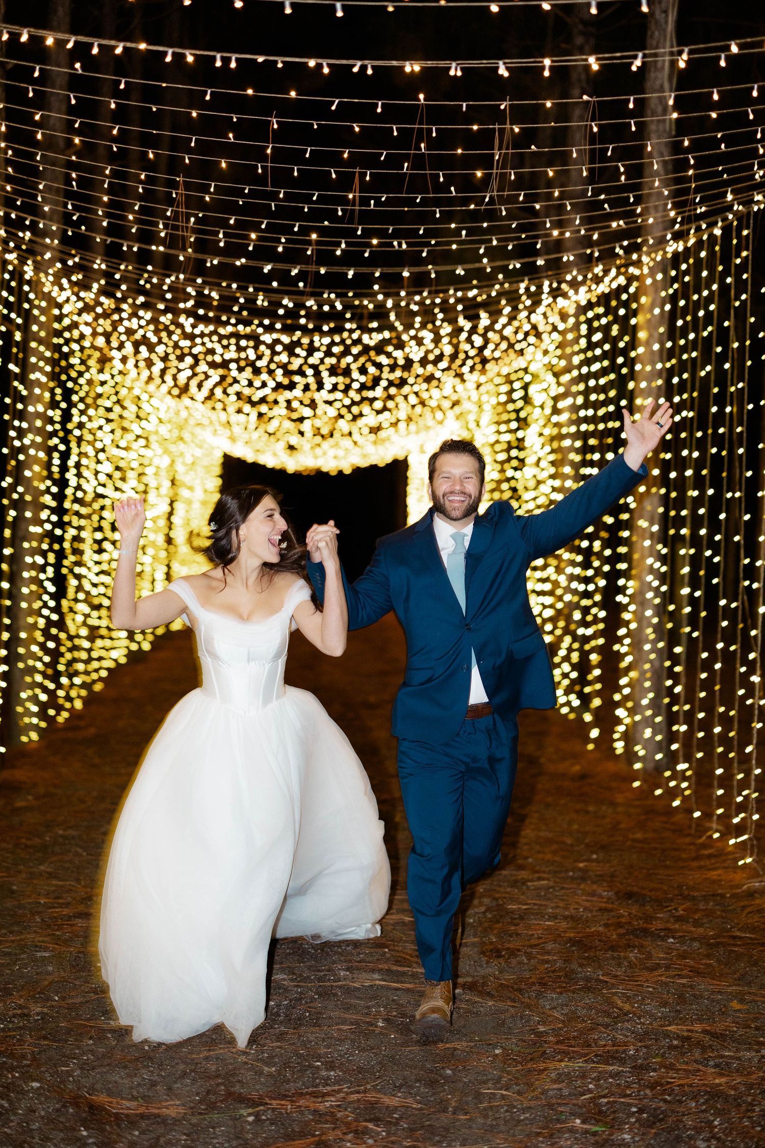 A couple dances joyfully under a magical canopy of twinkling string lights at an outdoor evening celebration.
