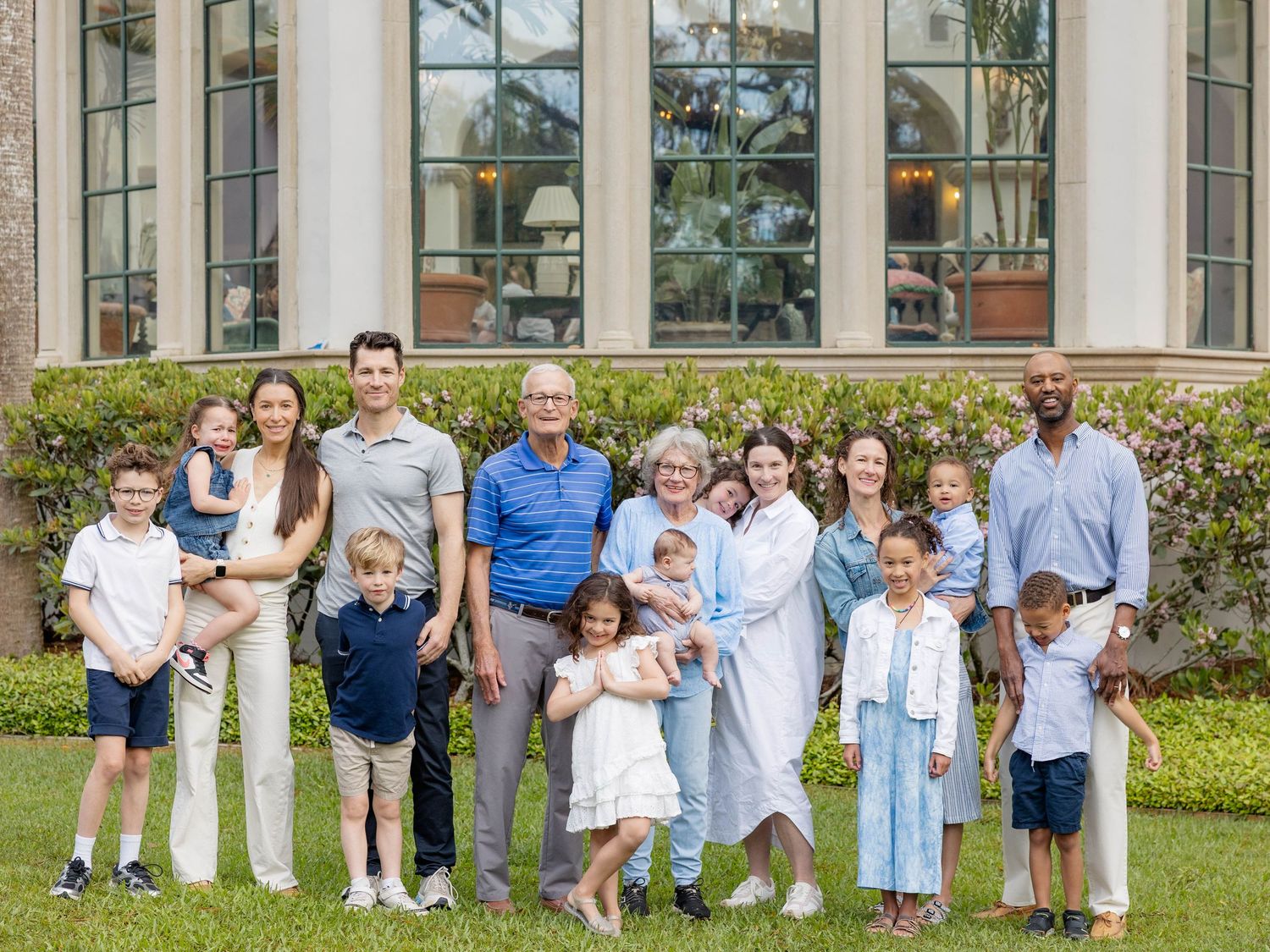 Large multigenerational family posing together outdoors on green lawn in front of elegant building.