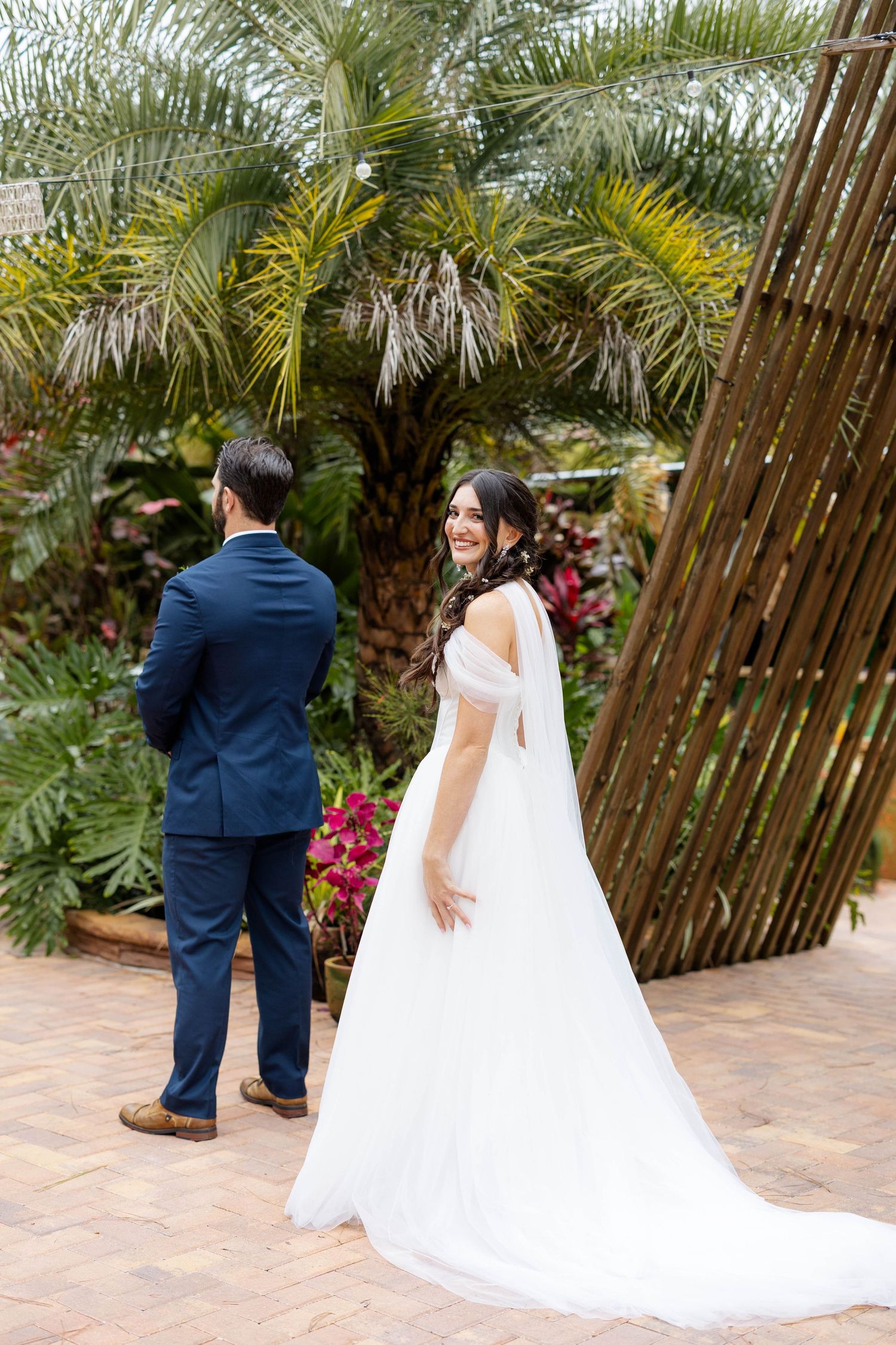 A romantic first look moment between a couple at a tropical wedding venue with palm trees and bamboo fencing.