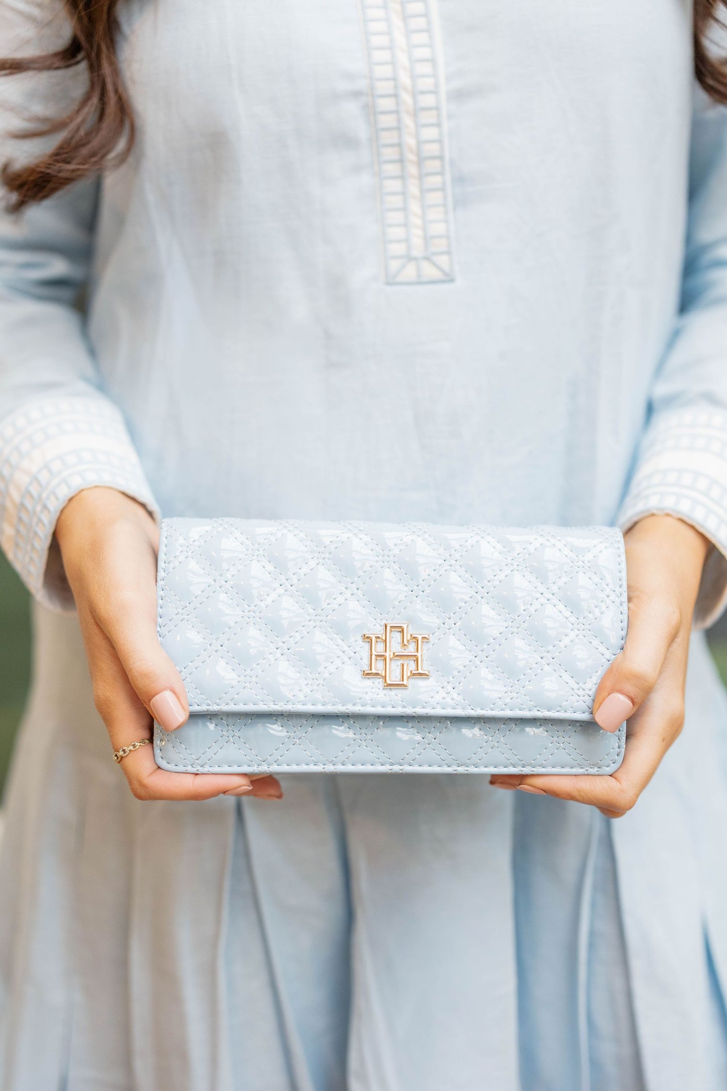 Woman in light blue dress holding a quilted baby blue clutch wallet with gold monogram hardware.