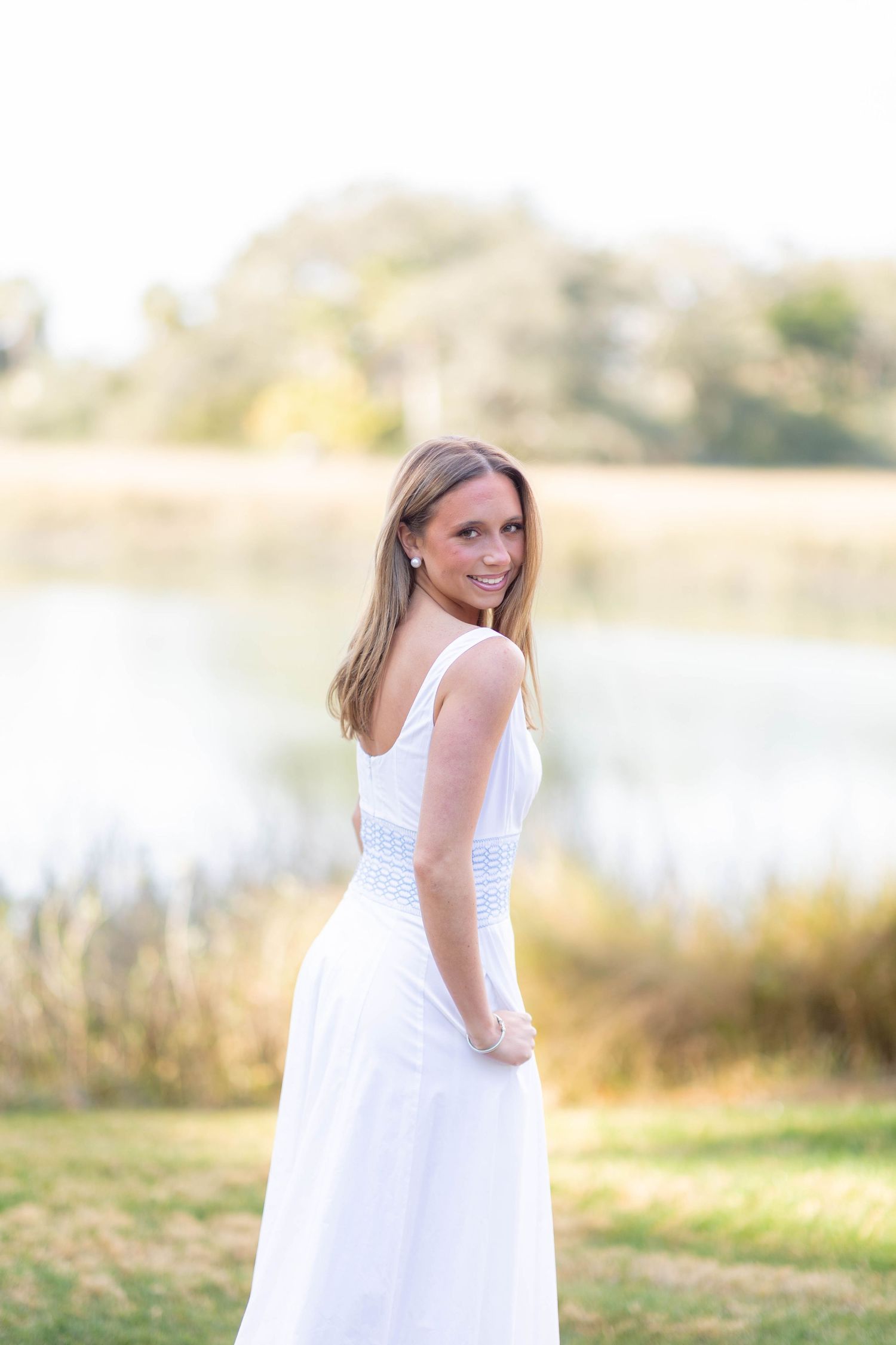 Person in white sundress posing by a lake during golden hour.