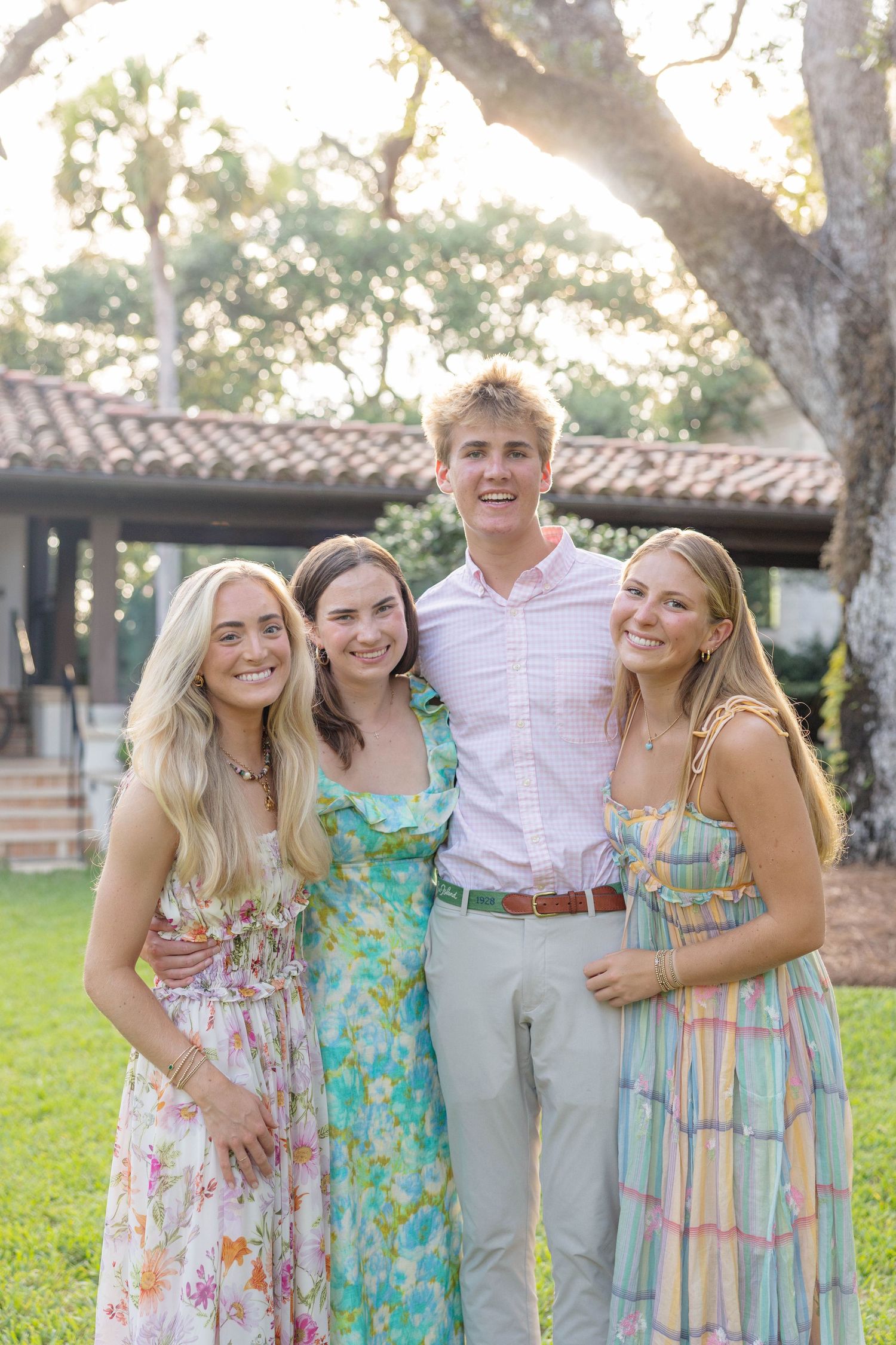 Four smiling young adults pose outdoors in colorful spring attire near a tree and building.