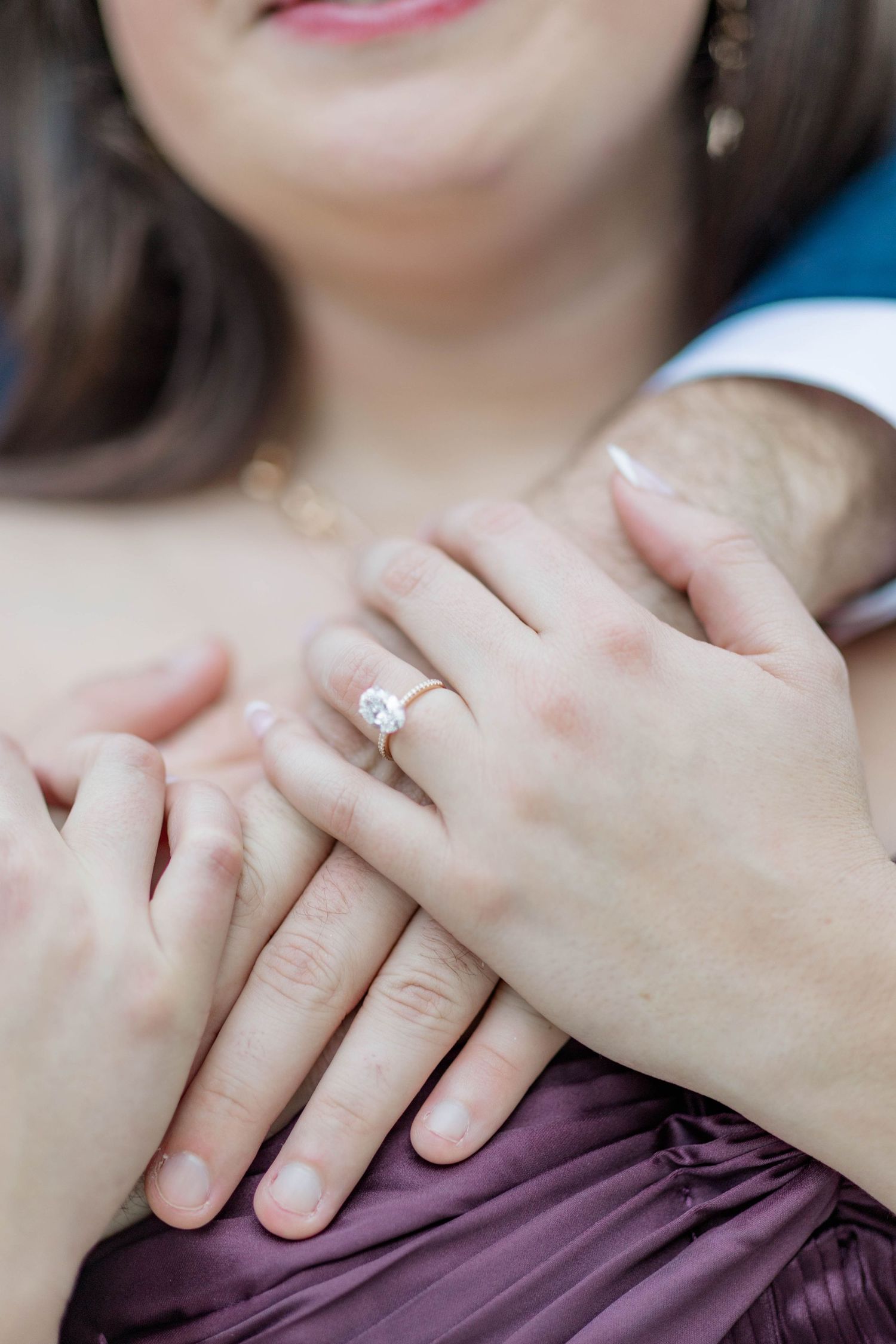 Close-up of a woman's hand displaying a solitaire diamond engagement ring while embracing her partner.