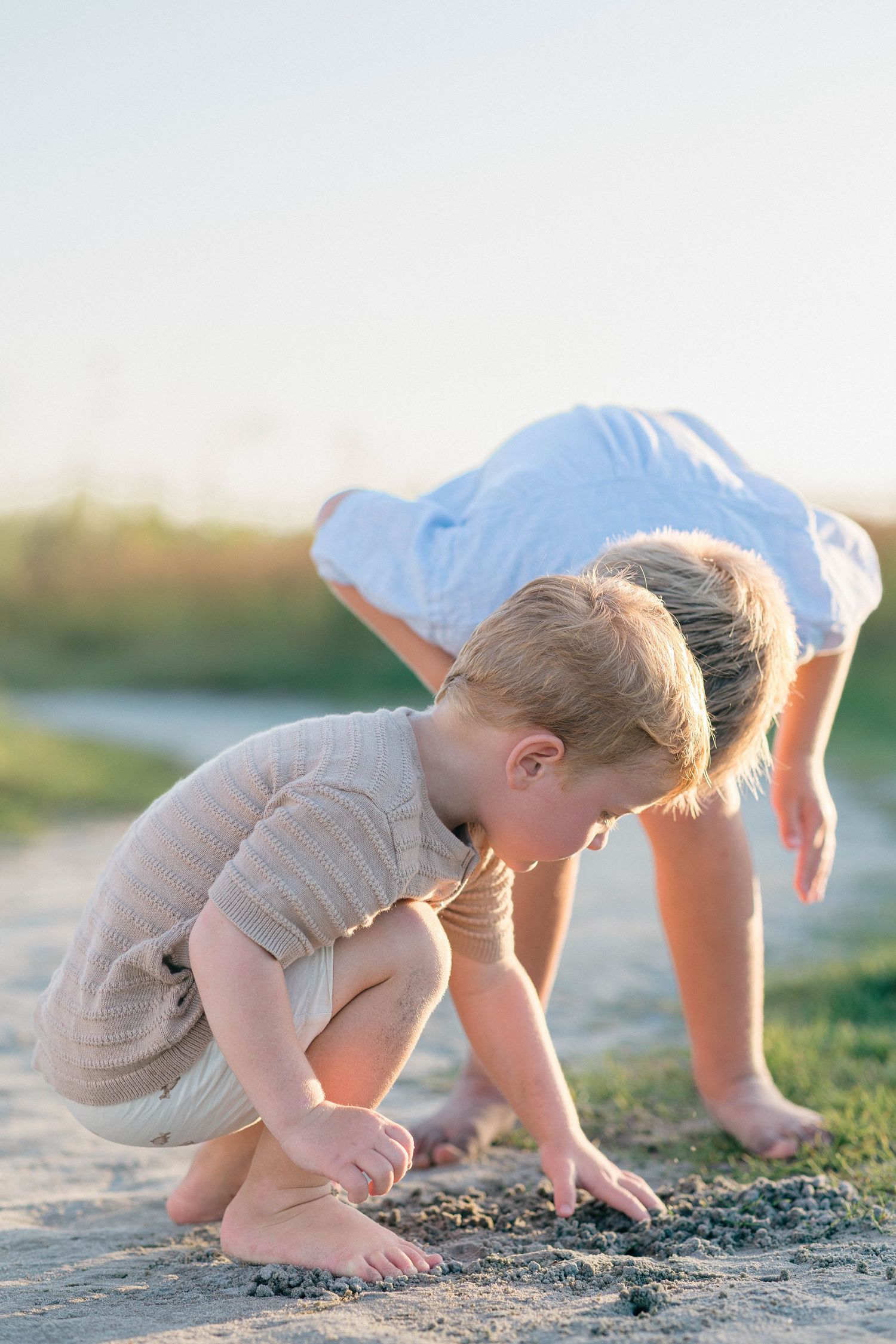 Two young barefoot children playing in sandy dirt outdoors during golden hour sunset light.