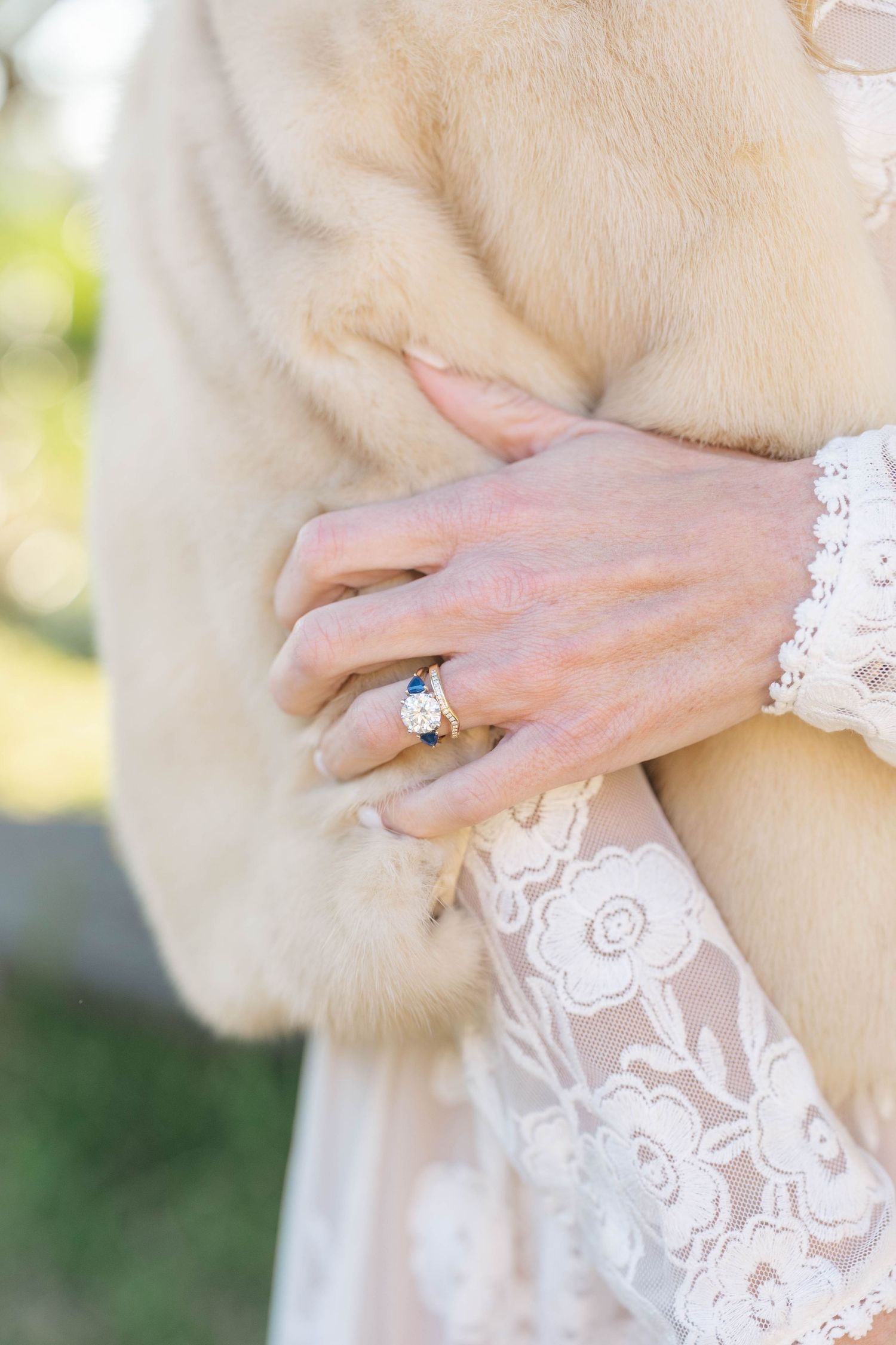 Close-up details of delicate white lace wedding dress fabric and engagement ring in natural outdoor lighting.