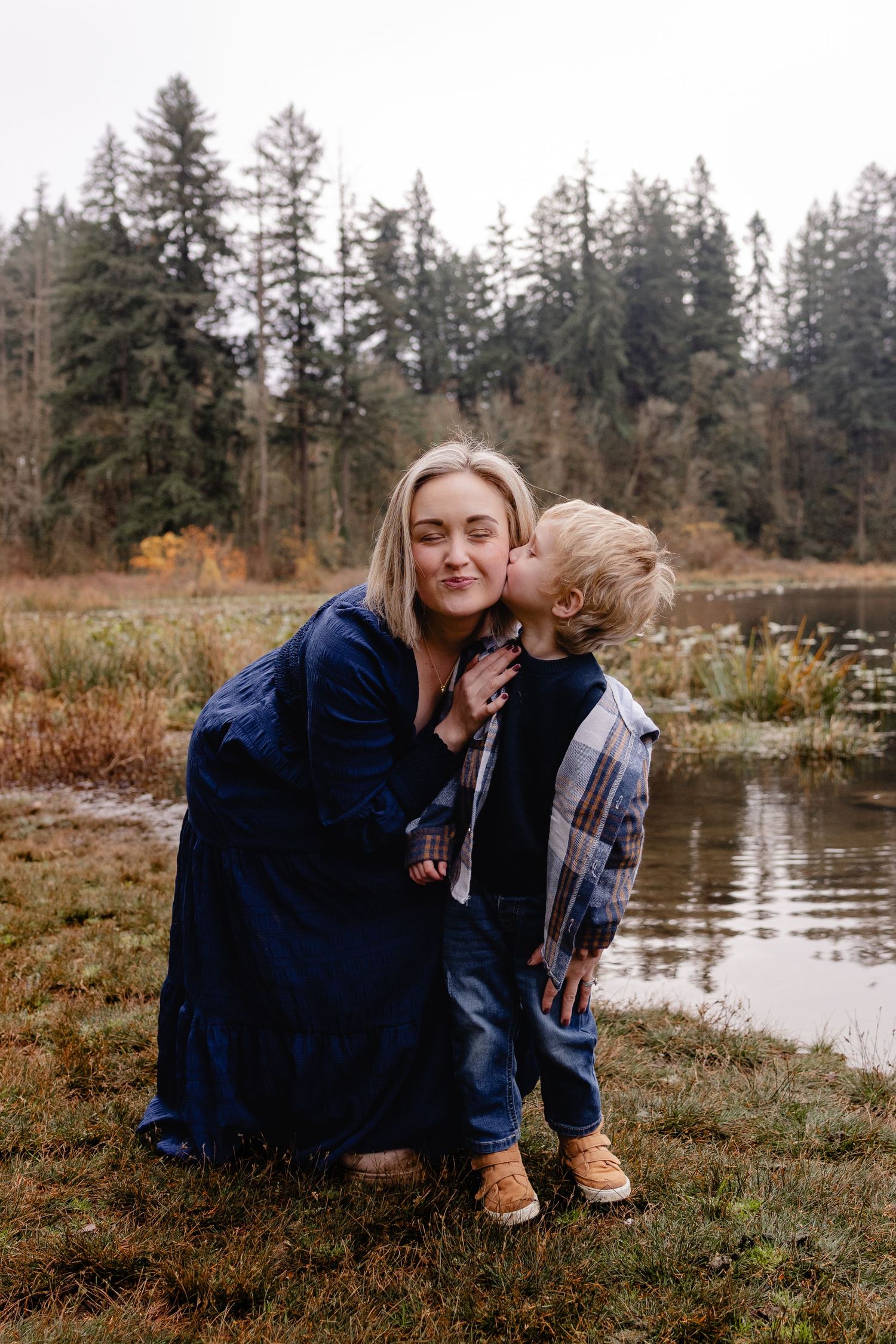 Blonde woman receiving a kiss from her young son by a lake.
