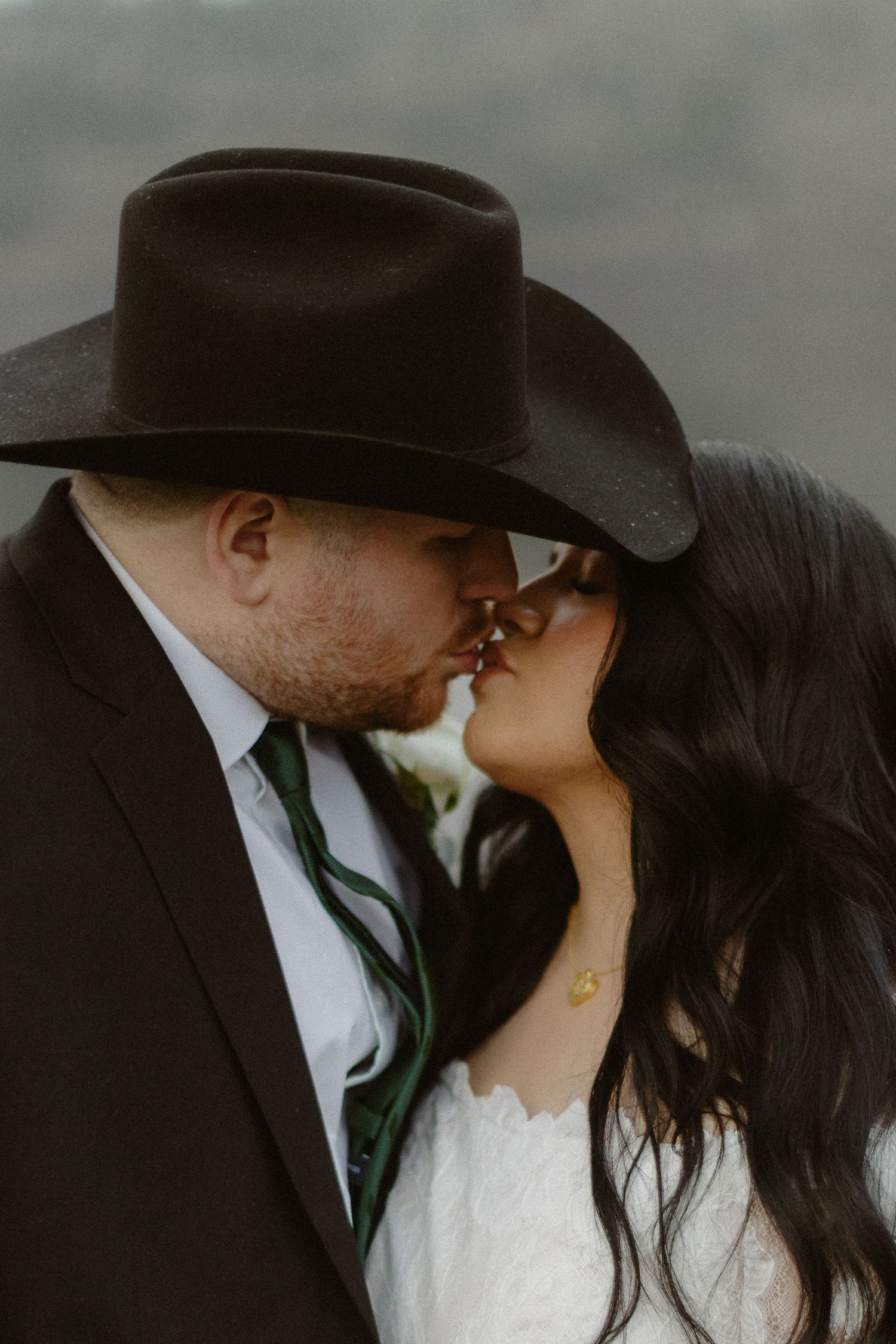 Close-up of bride and groom sharing a kiss, groom wearing a black cowboy hat on wedding day.