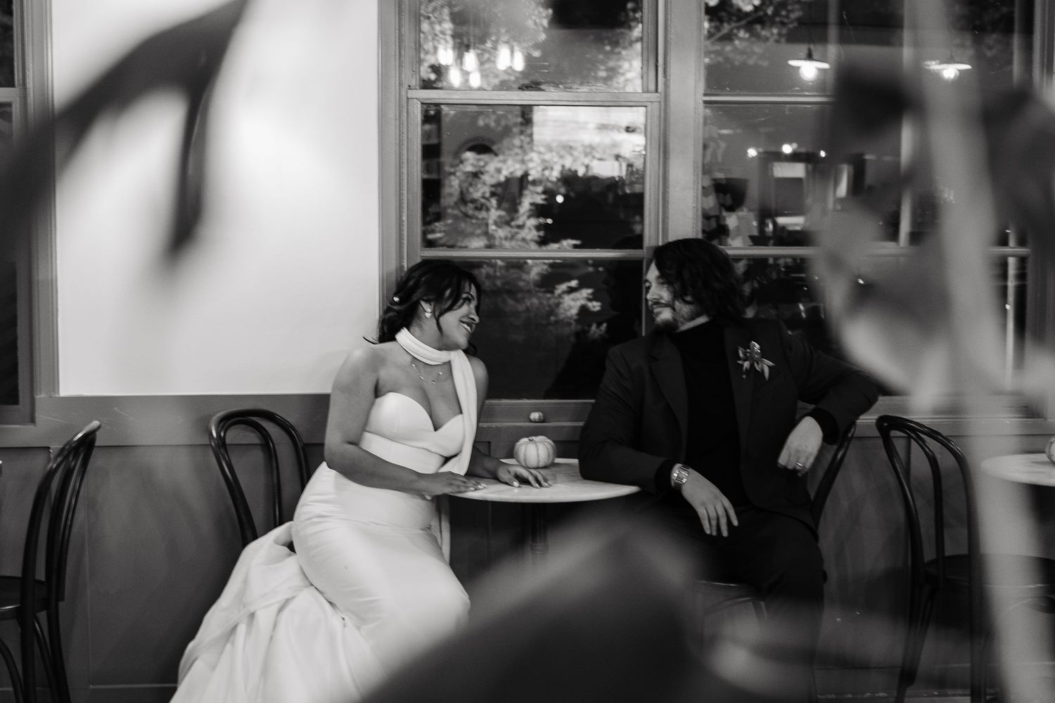 Black and white photo of bride and groom sitting at cafe table, sharing a moment.