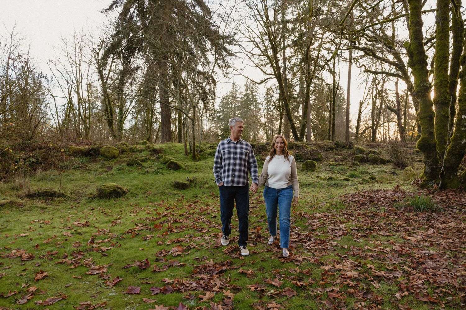 Couple holding hands walking through lush green mossy woodland forest together.