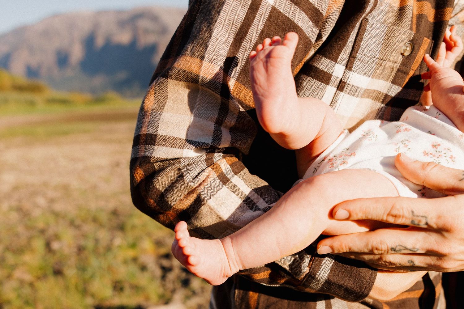 Close-up of a parent in plaid shirt cradling a newborn baby outdoors.