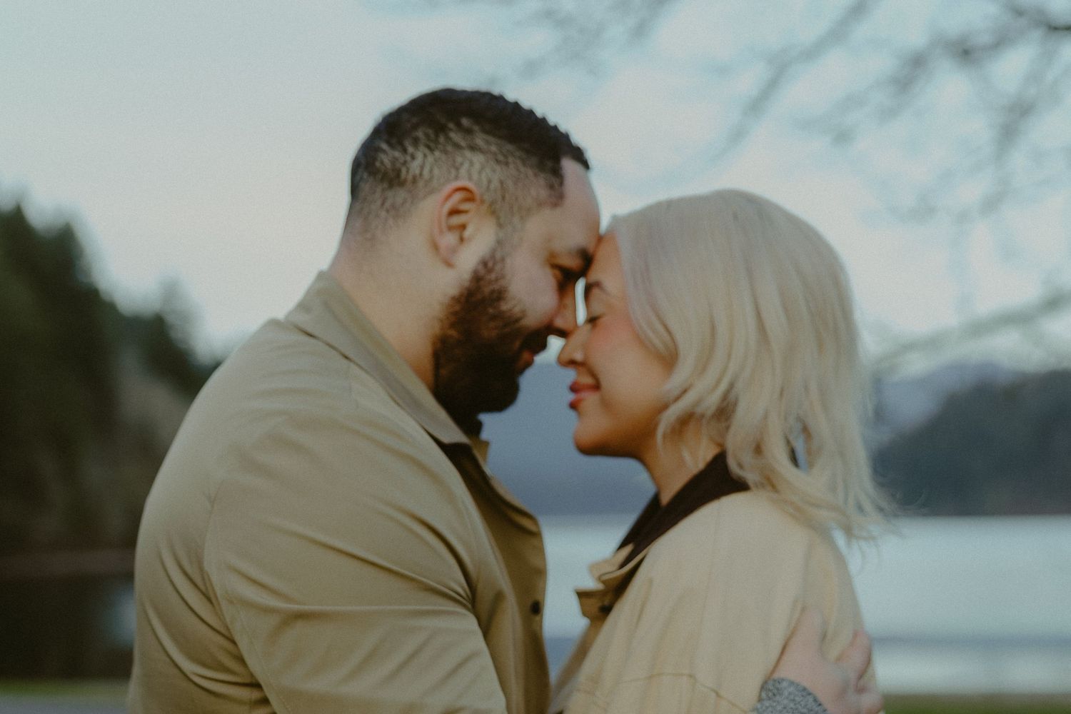 Romantic couple touching foreheads intimately near a lake at dusk.