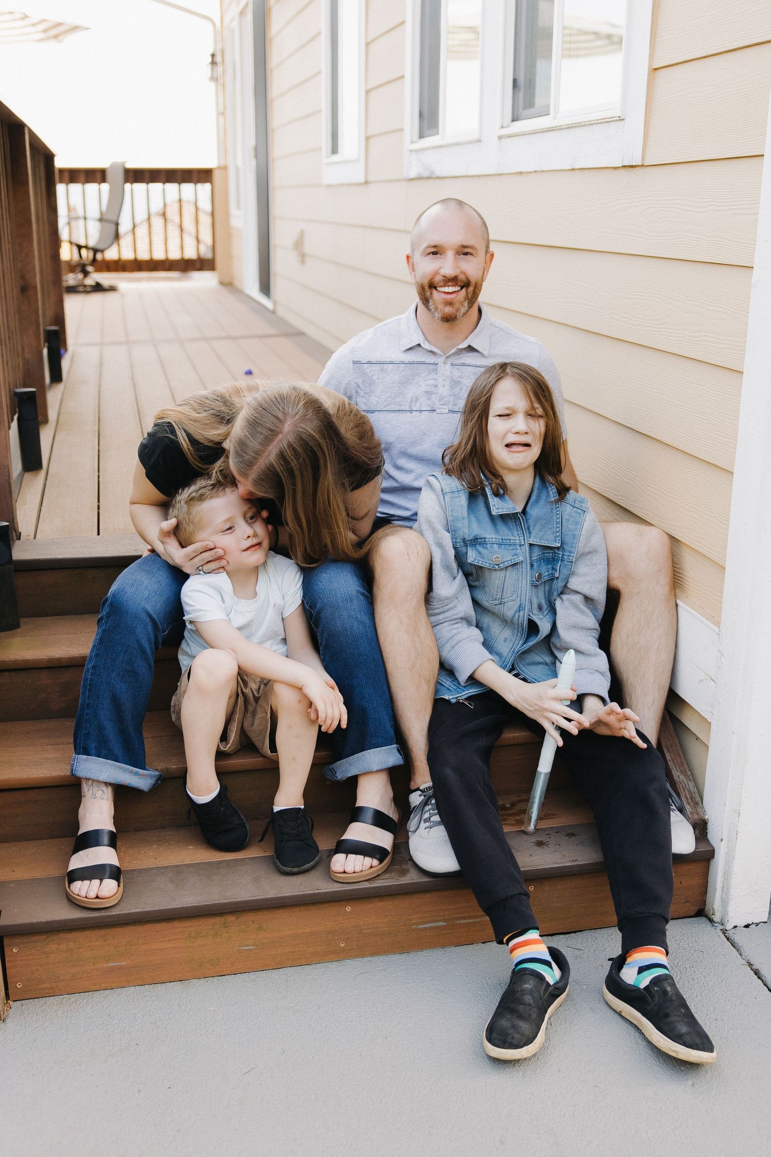 Family of four sitting on outdoor steps, sharing a joyful and playful moment together.