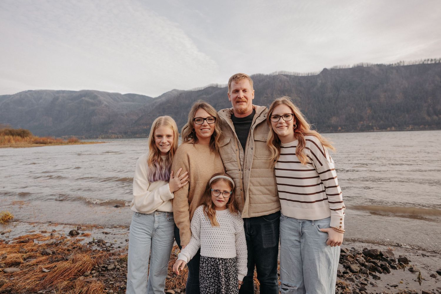 Happy family of five posing together by a mountain lake on an overcast fall day.