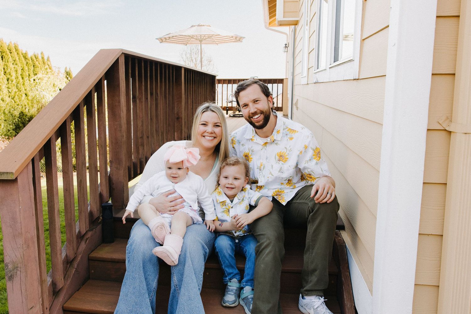 Happy family of four posing on wooden deck steps outside their home on sunny day.